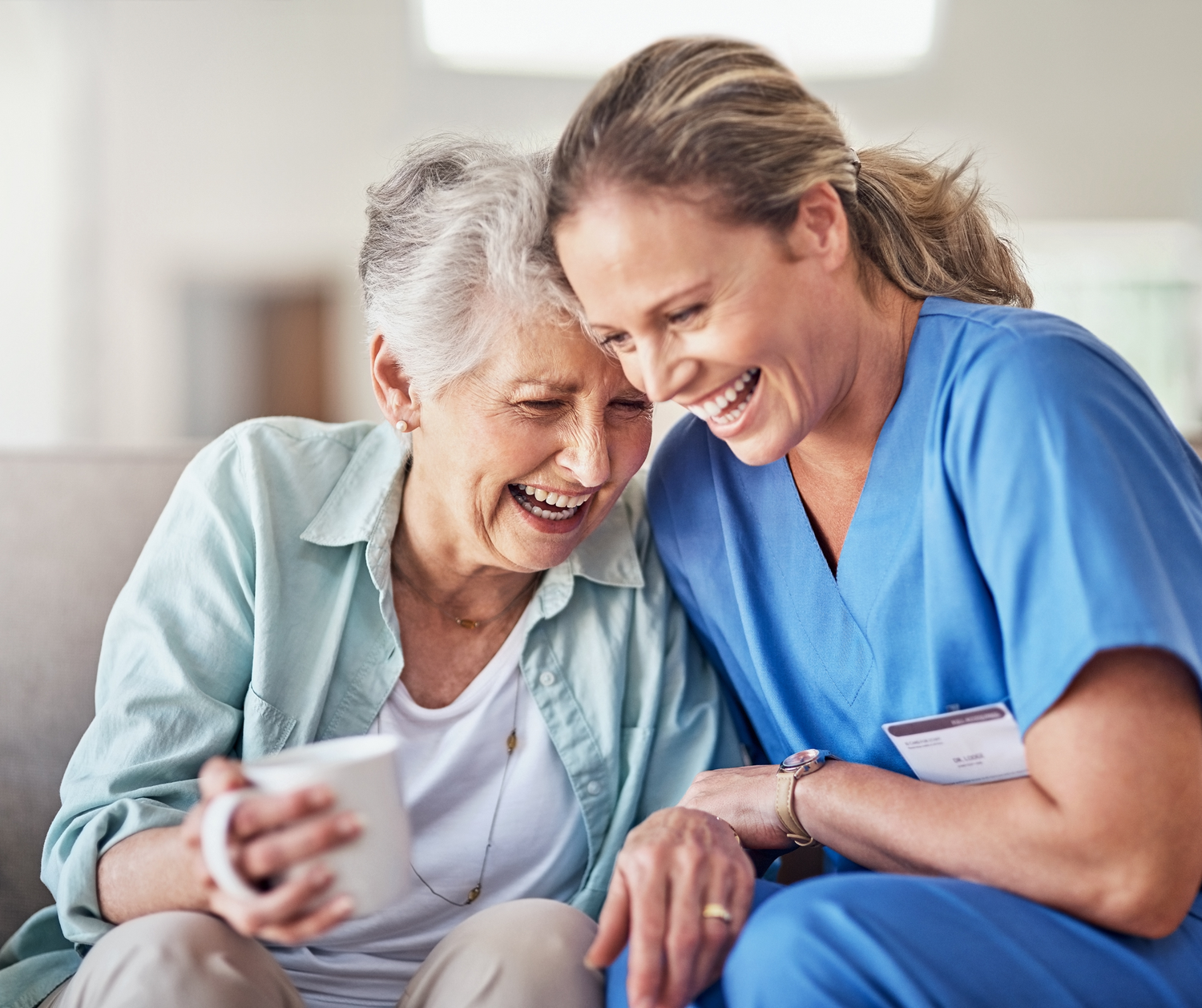Healthcare worker in blue scrubs shares joyful moments with elderly patient in assisted living facility.