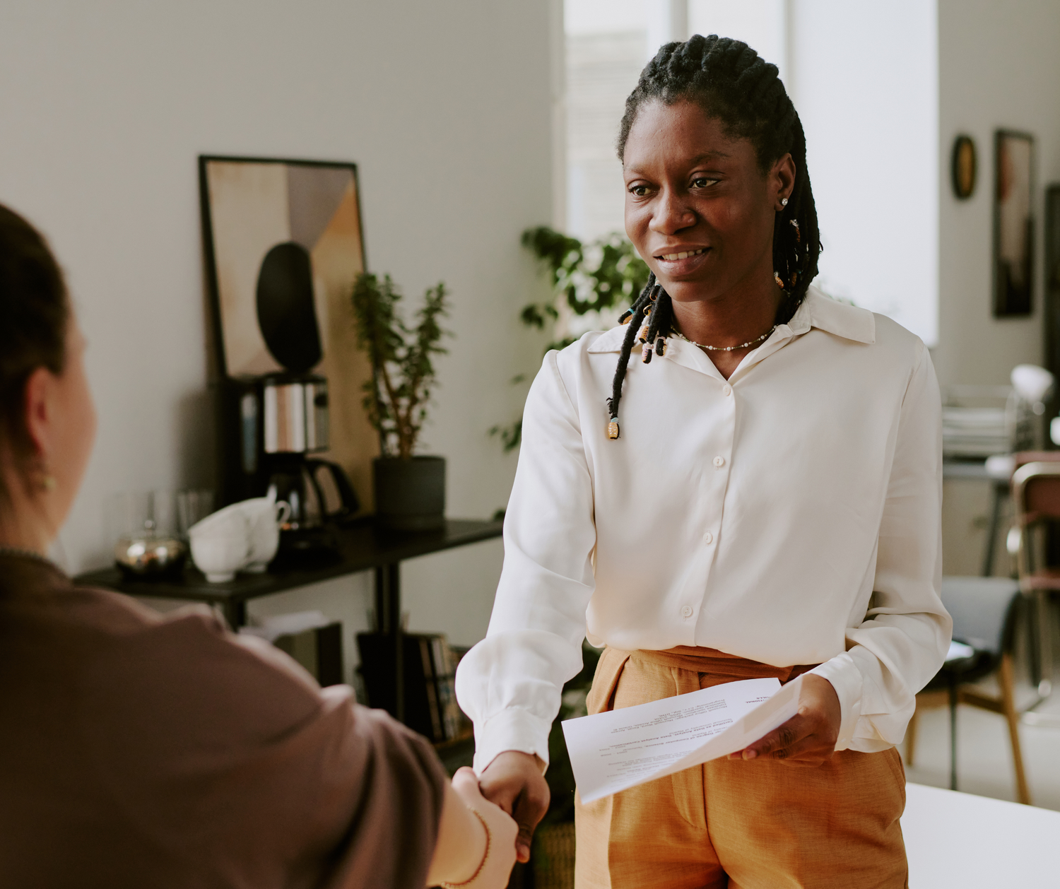 Professional in a white shirt and brown pants shaking hands with interviewer in a modern office setting.