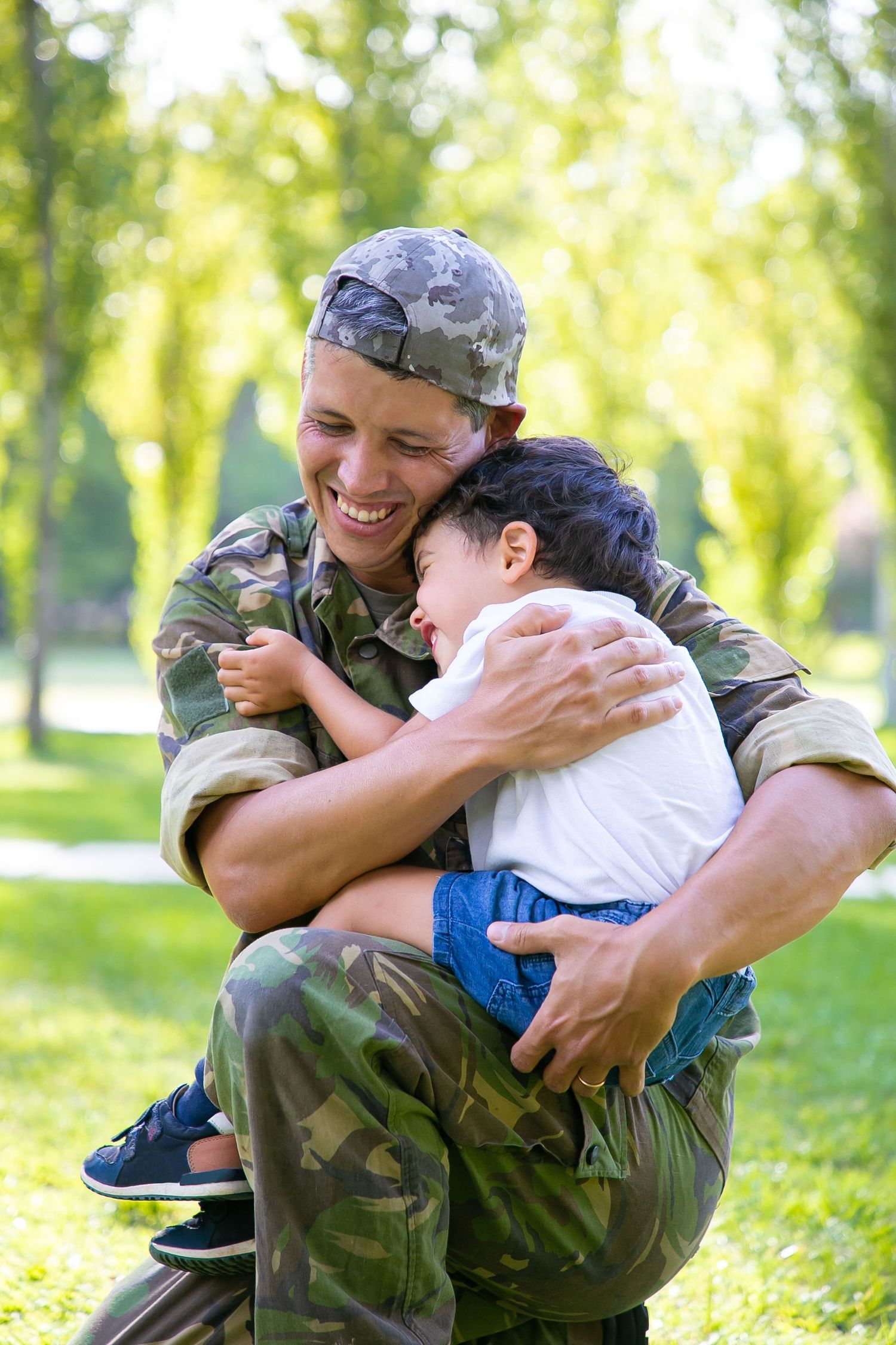A joyful reunion between a soldier in camouflage uniform and a young child in a park setting.