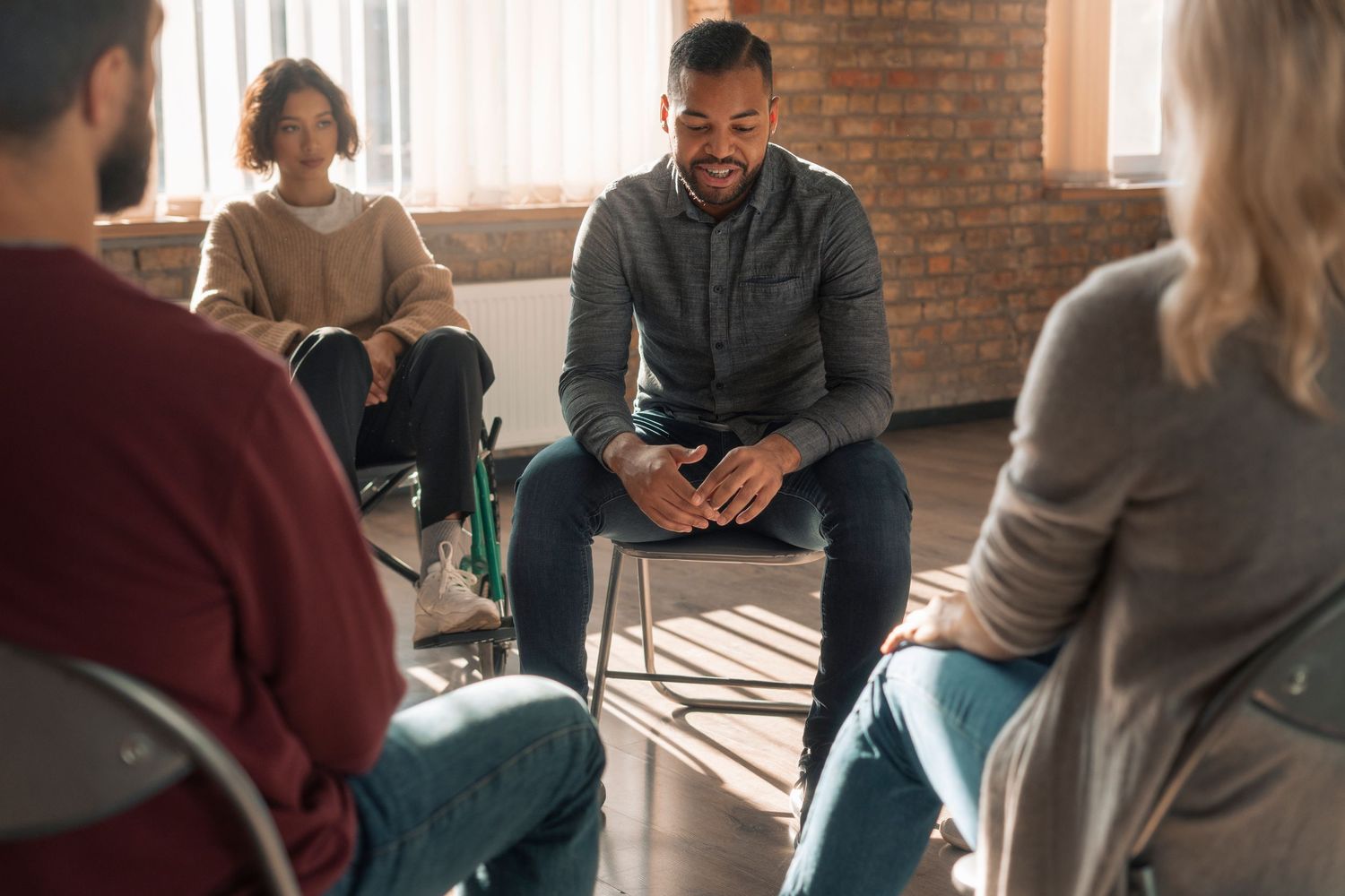 People sit in a circle during a group therapy or counseling session in a modern office with brick walls.