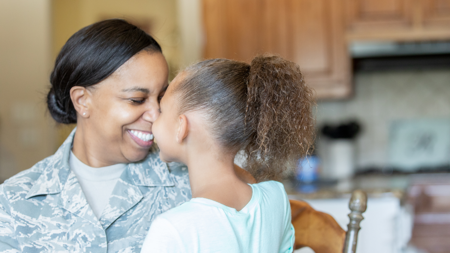 A military mother and daughter shares intimate moment together in photo showing affection and laughter.