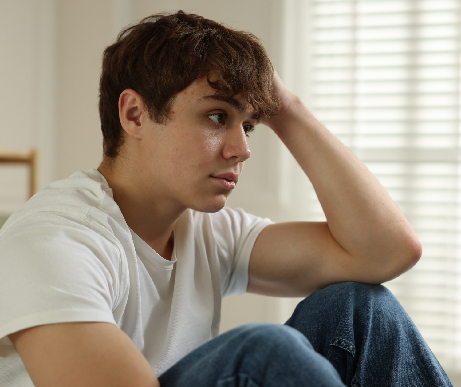 Person in white t-shirt and jeans sits on floor against wall being upset but getting help.