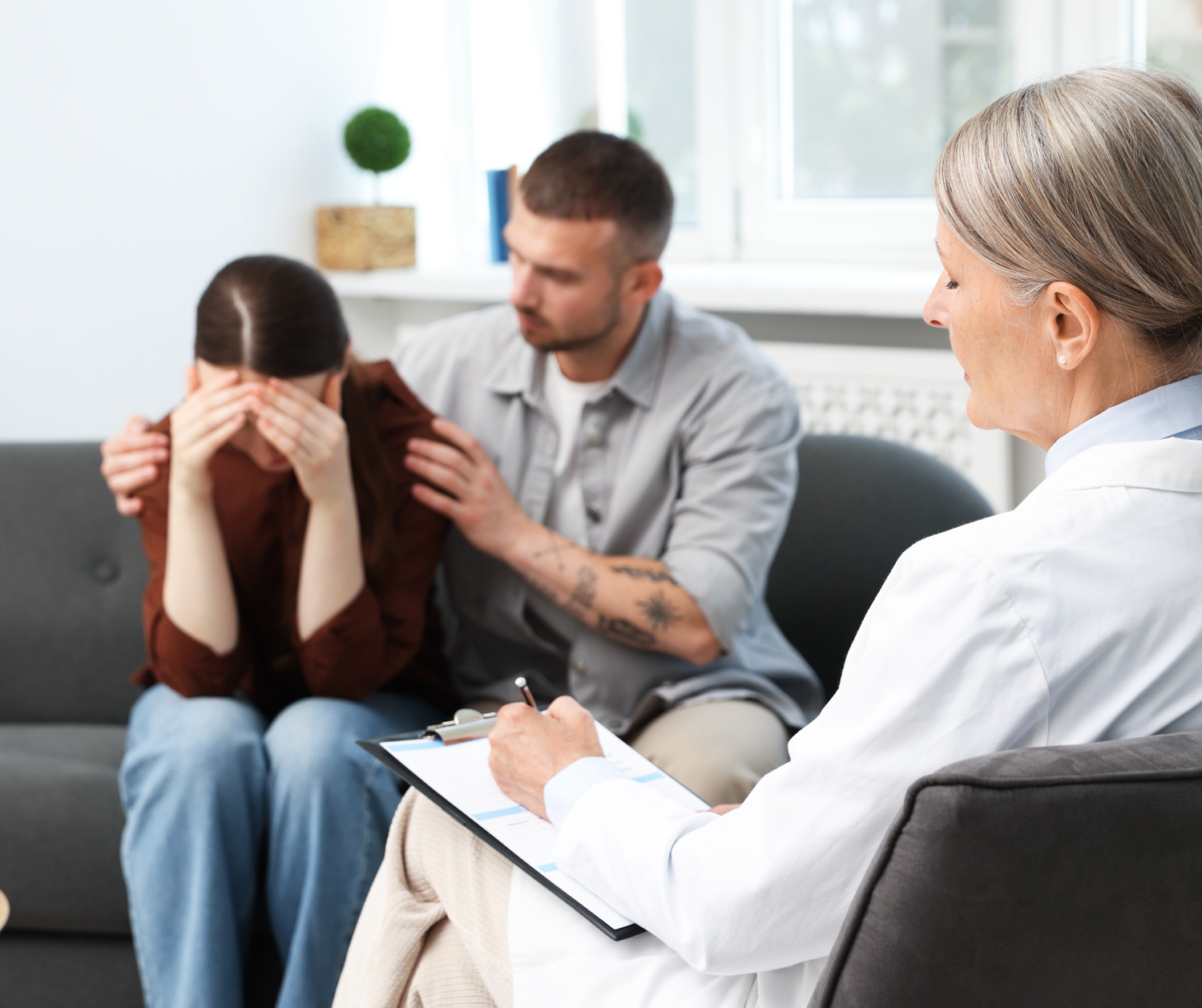Professional therapist taking notes while listening to patient during counseling session in modern office.