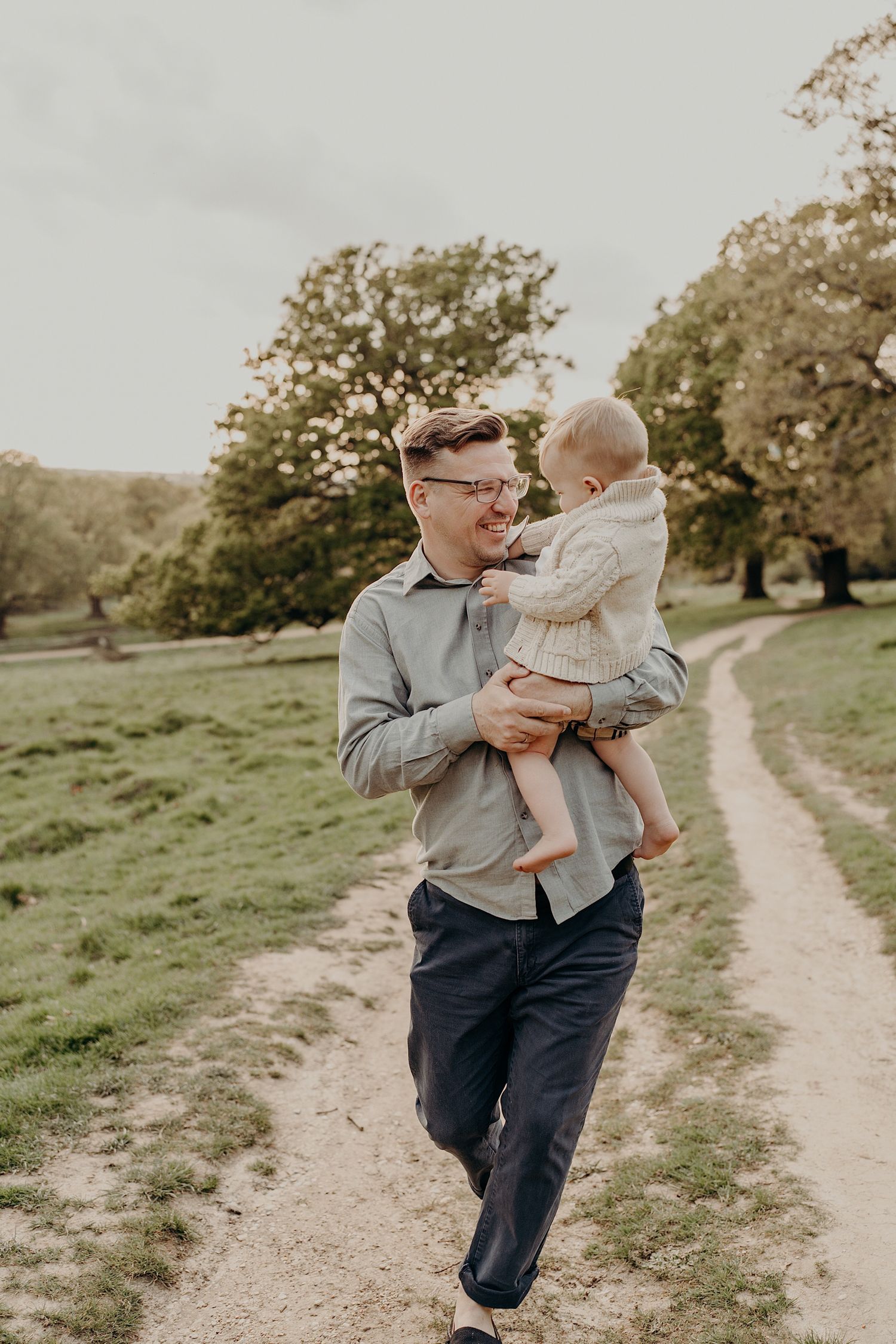 Playful interaction between adult and child on a scenic dirt path surrounded by greenery.