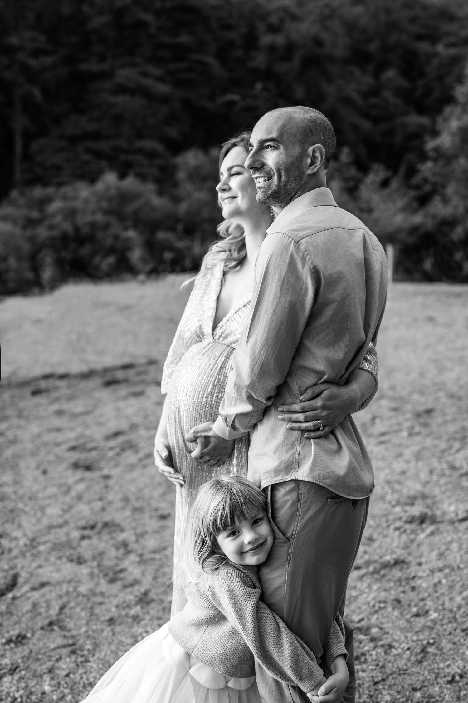 Black and white photo of family embracing outdoors on grassy hillside.