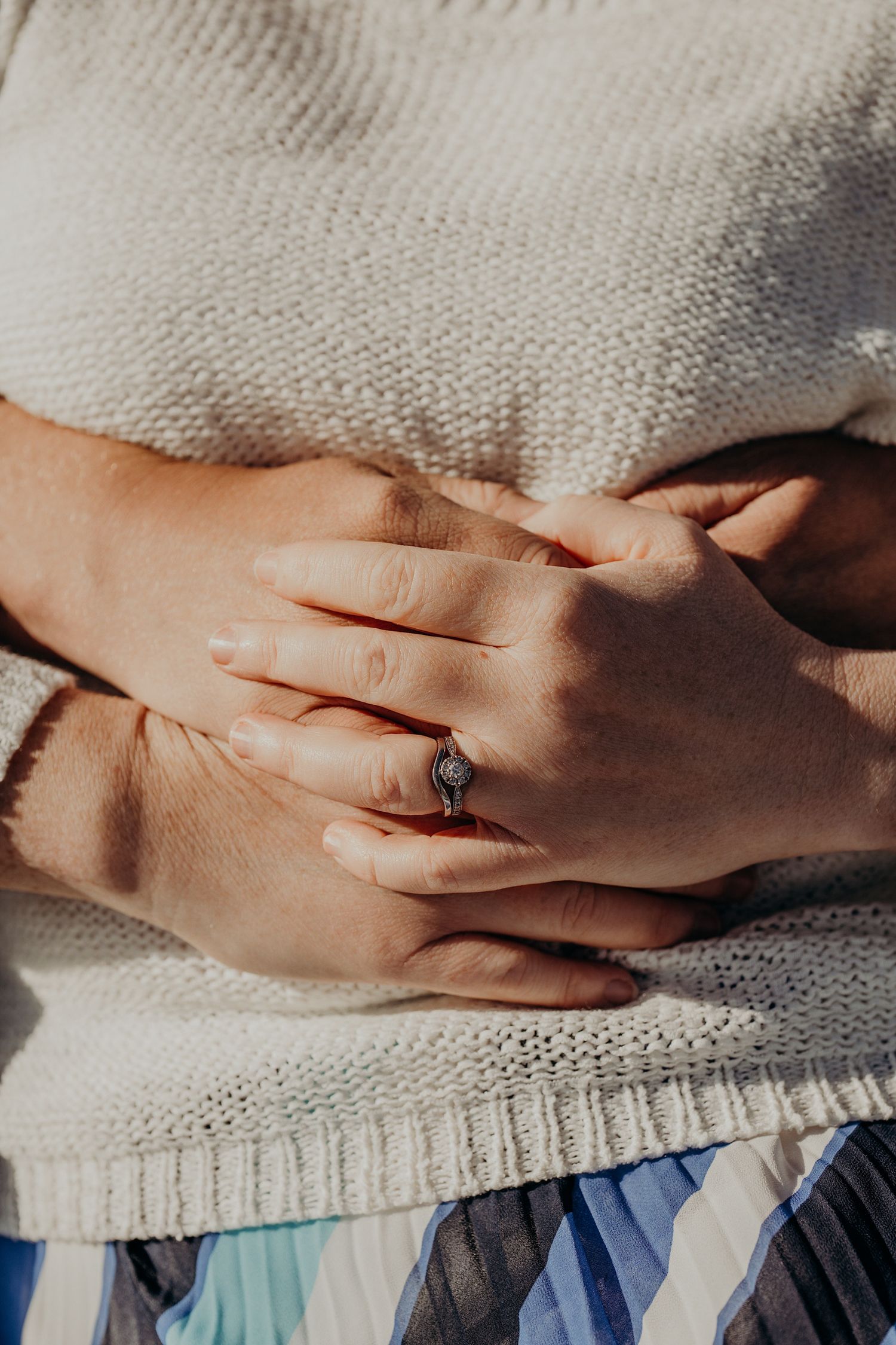 Hands with engagement ring clasped together on knit fabric.