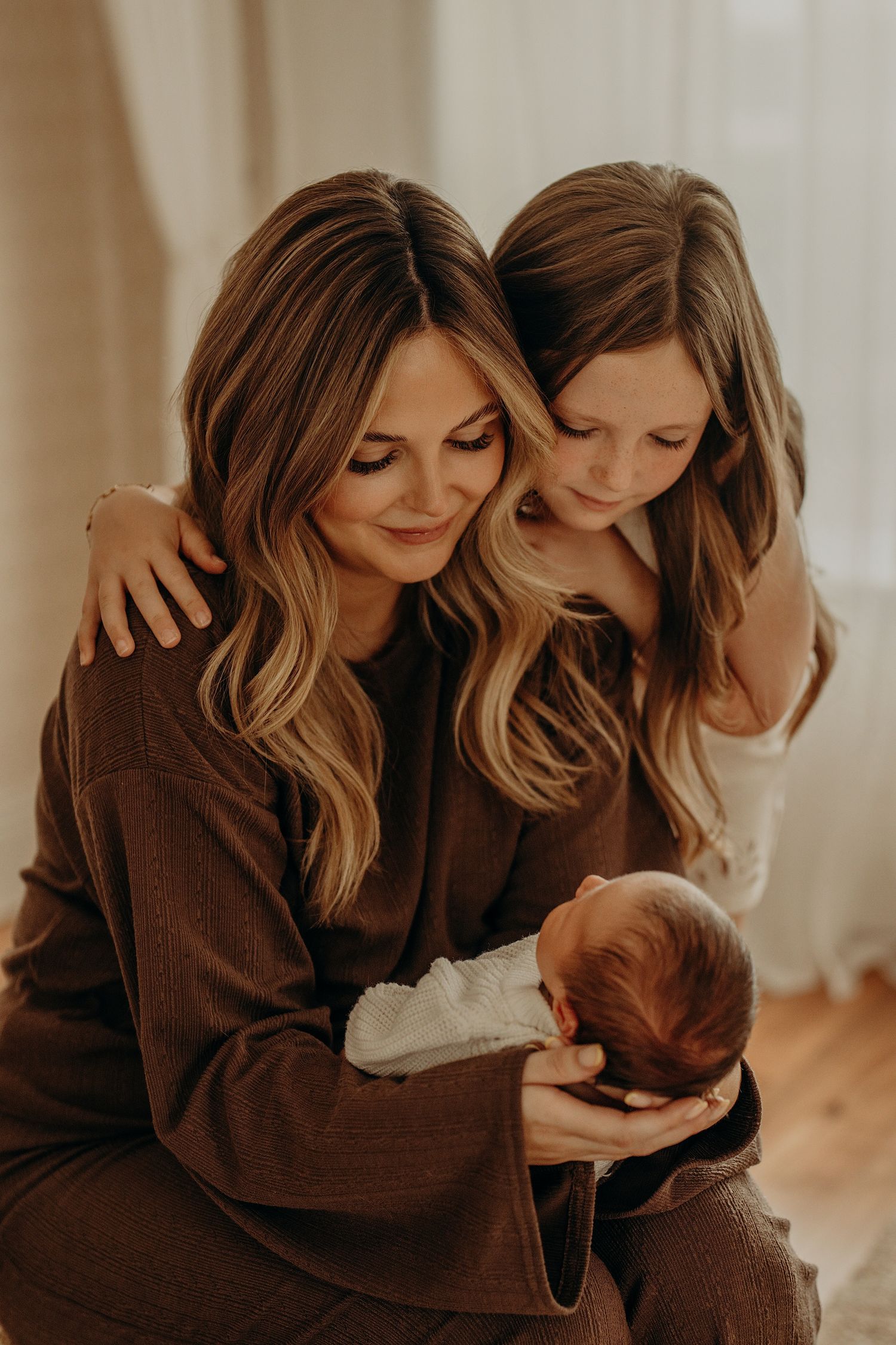 Mother and daughter sharing intimate moment in warm brown tones during lifestyle photoshoot.