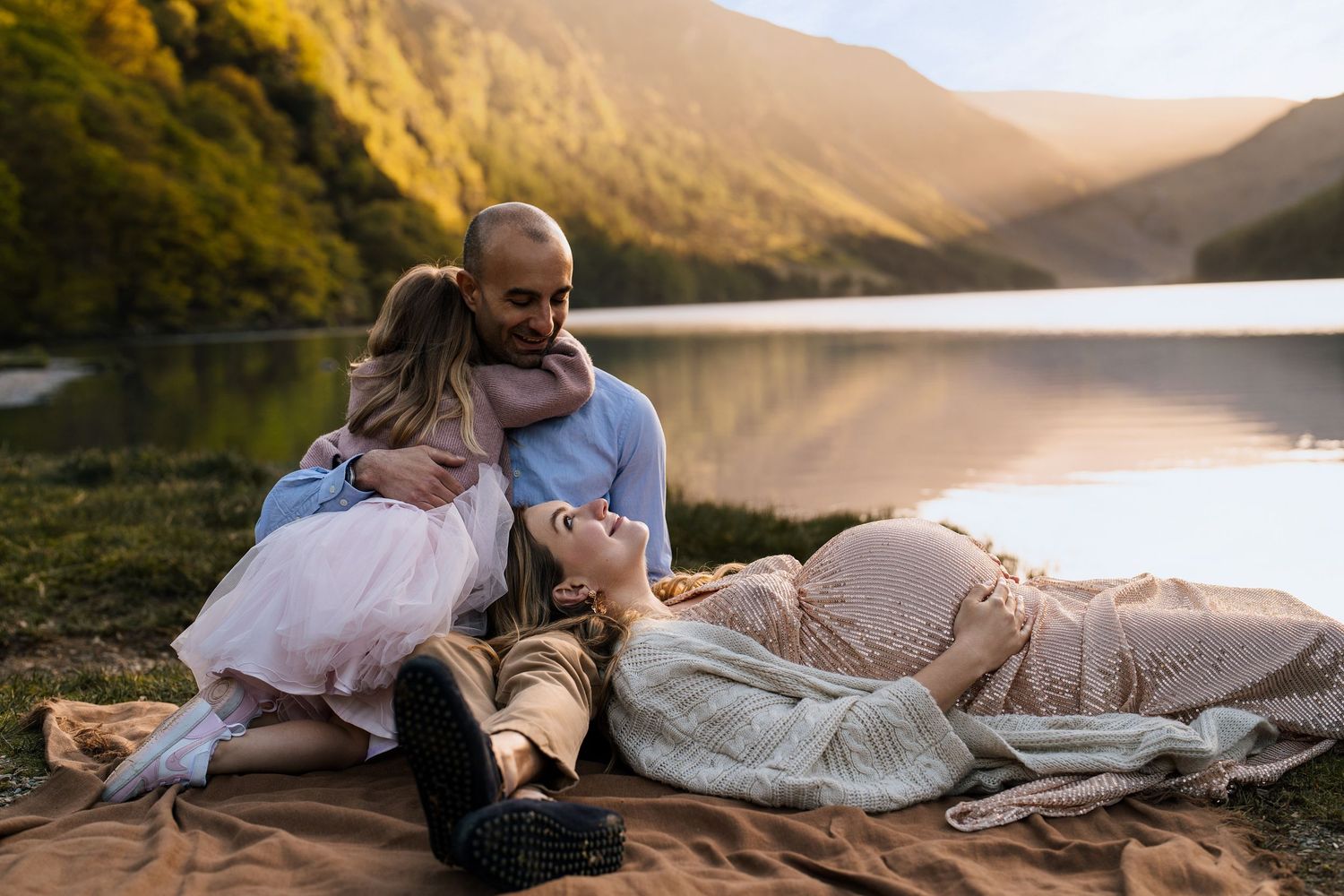 Romantic maternity photos taken at sunset by a lake with mountain views.