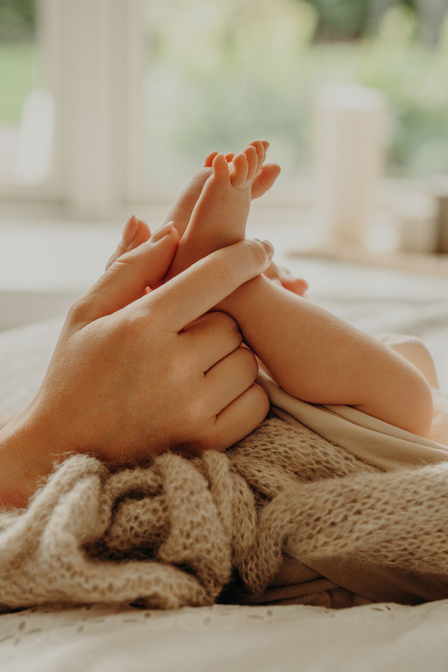 Tiny baby feet resting on knitted beige blanket in natural window light.