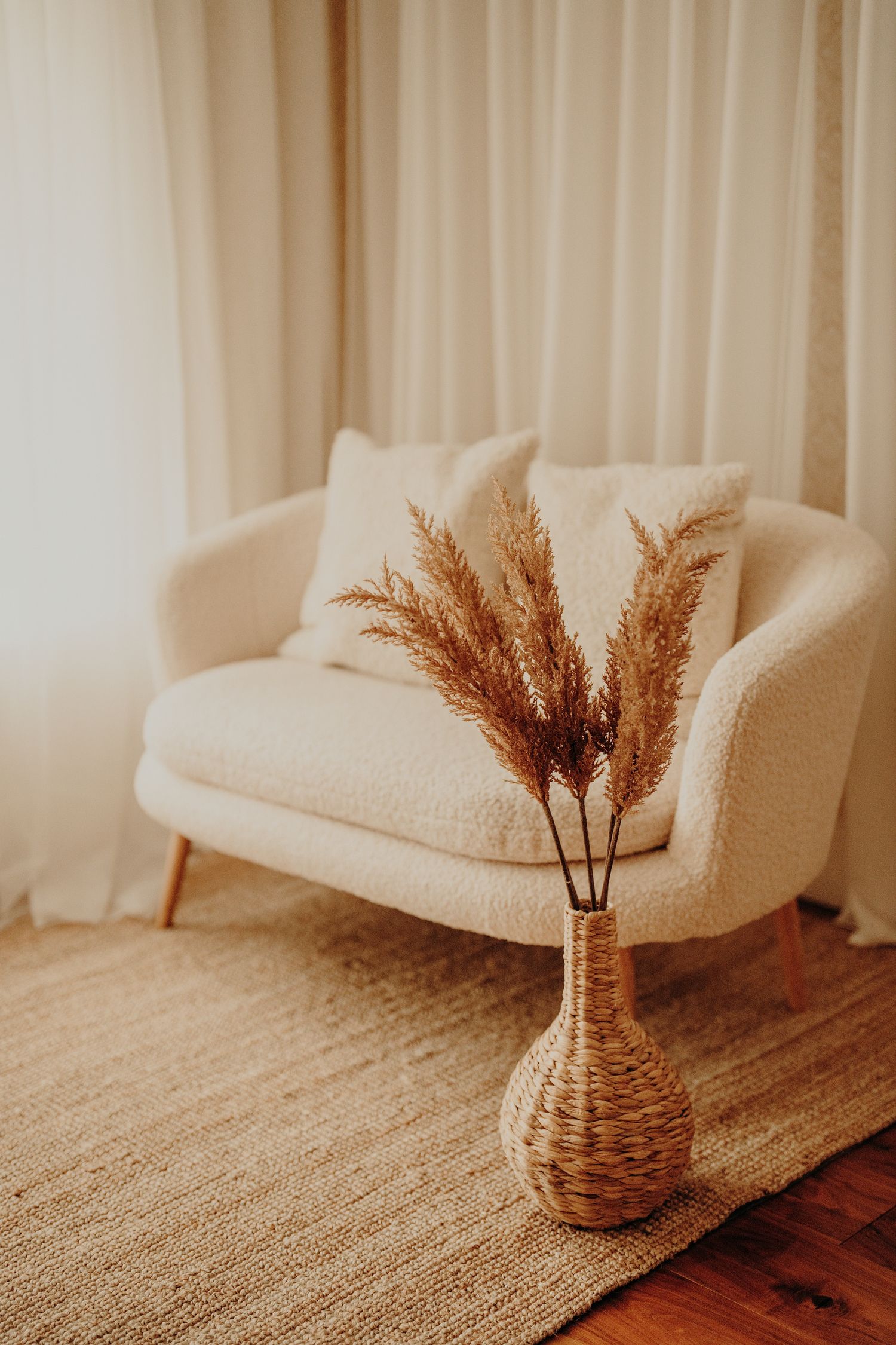 Minimalist interior with beige couch and dried pampas grass in woven vase.