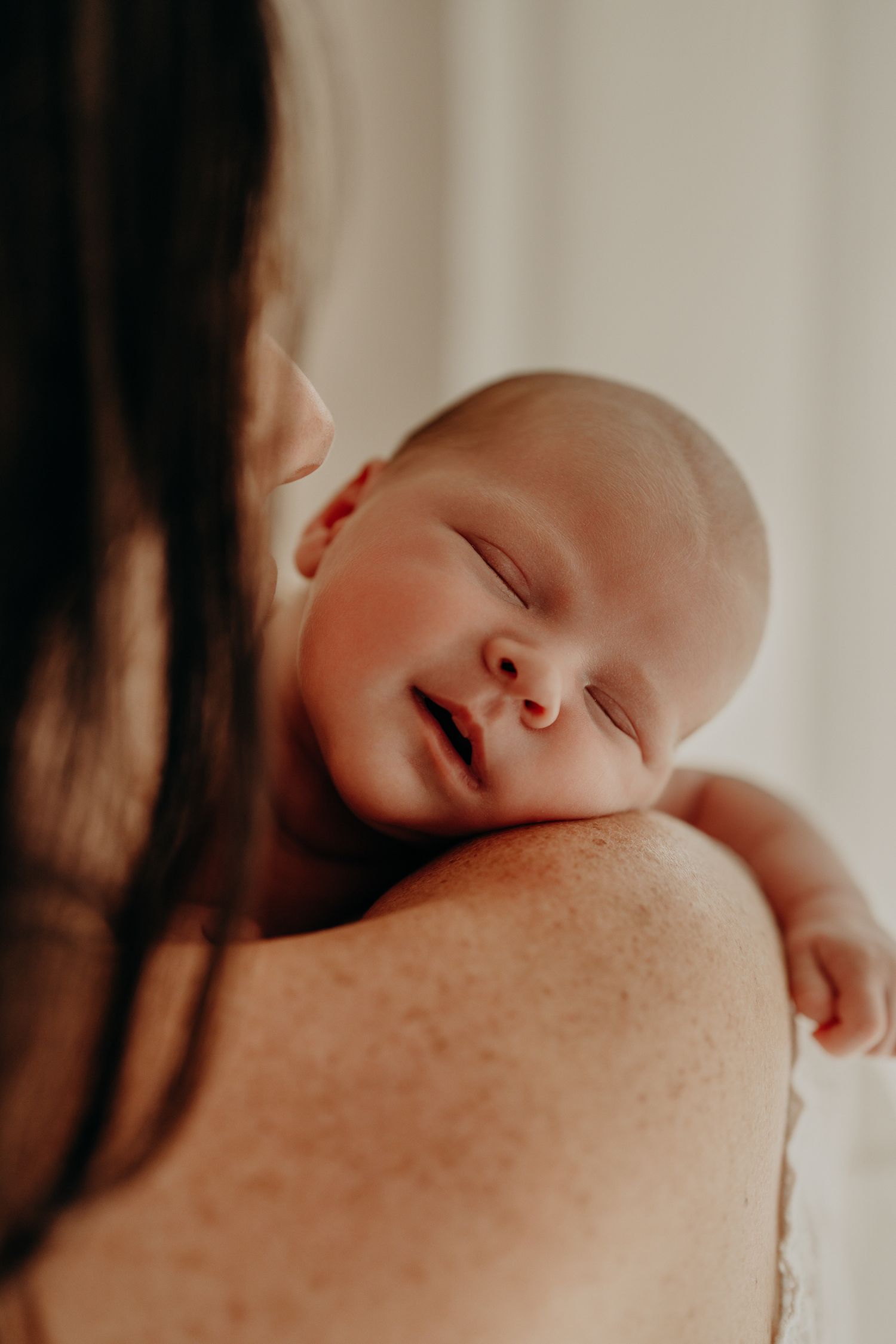 Peaceful sleeping newborn resting on shoulder in gentle natural light.