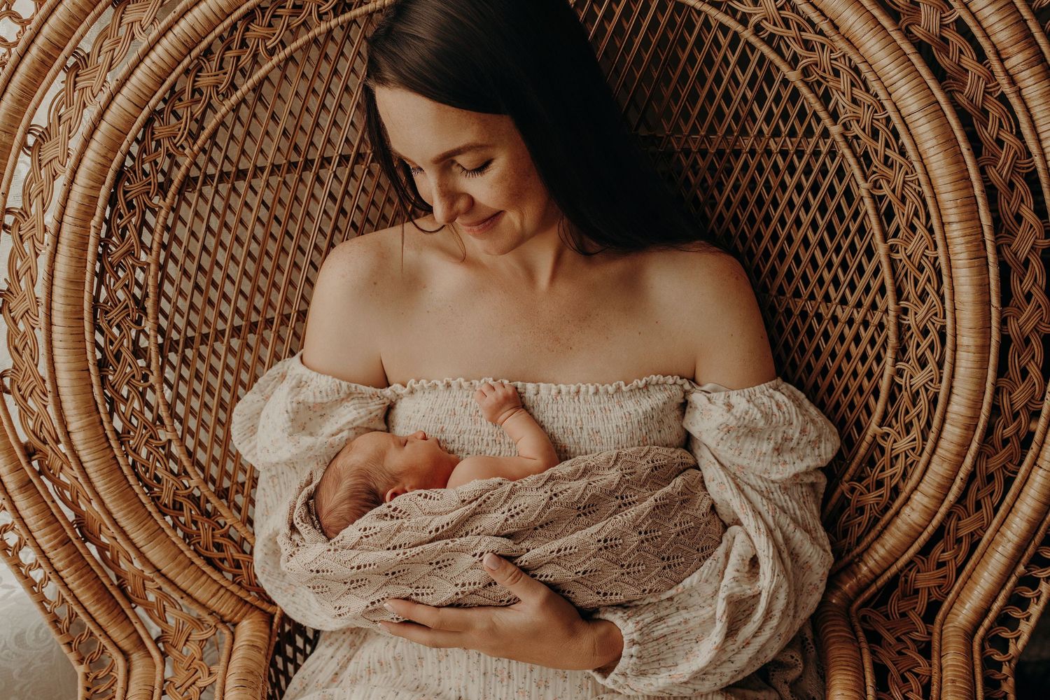 Intimate newborn photography session with baby resting in a woven wicker chair.
