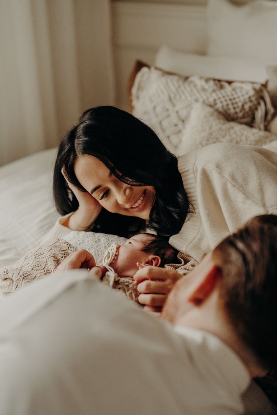 Close-up of tender family moment with baby on white bedding in muted tones.