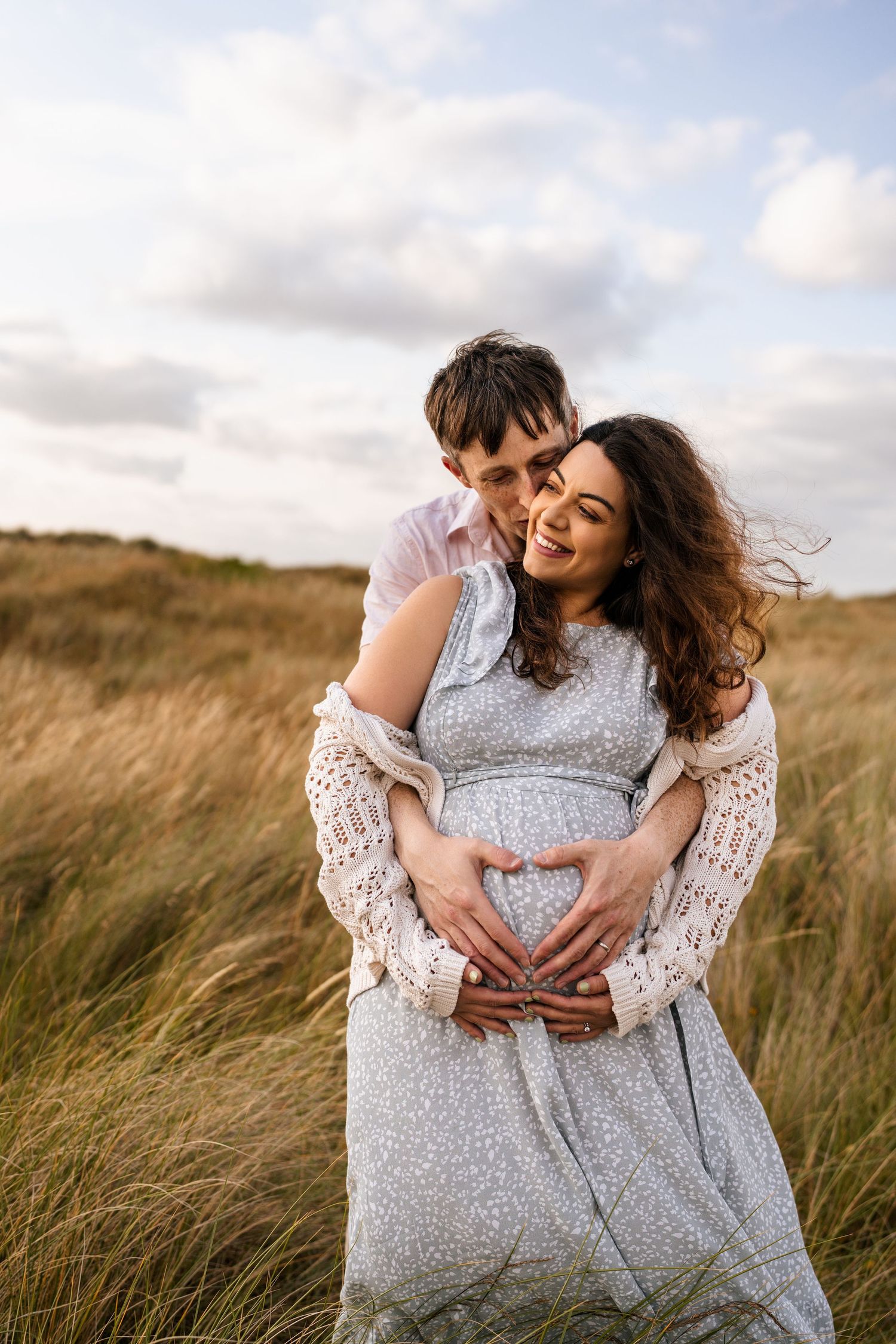 Couple embracing in tall grass field during golden hour maternity photoshoot.