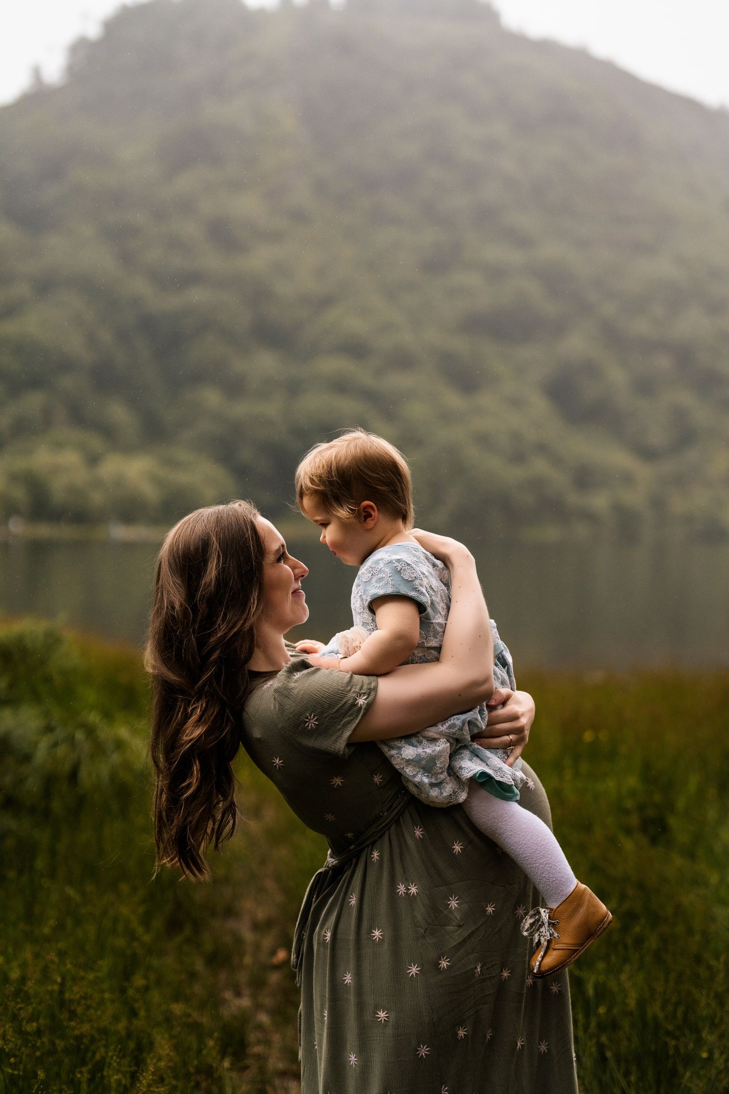 A playful scene of mother and child embracing by a scenic mountain lake.