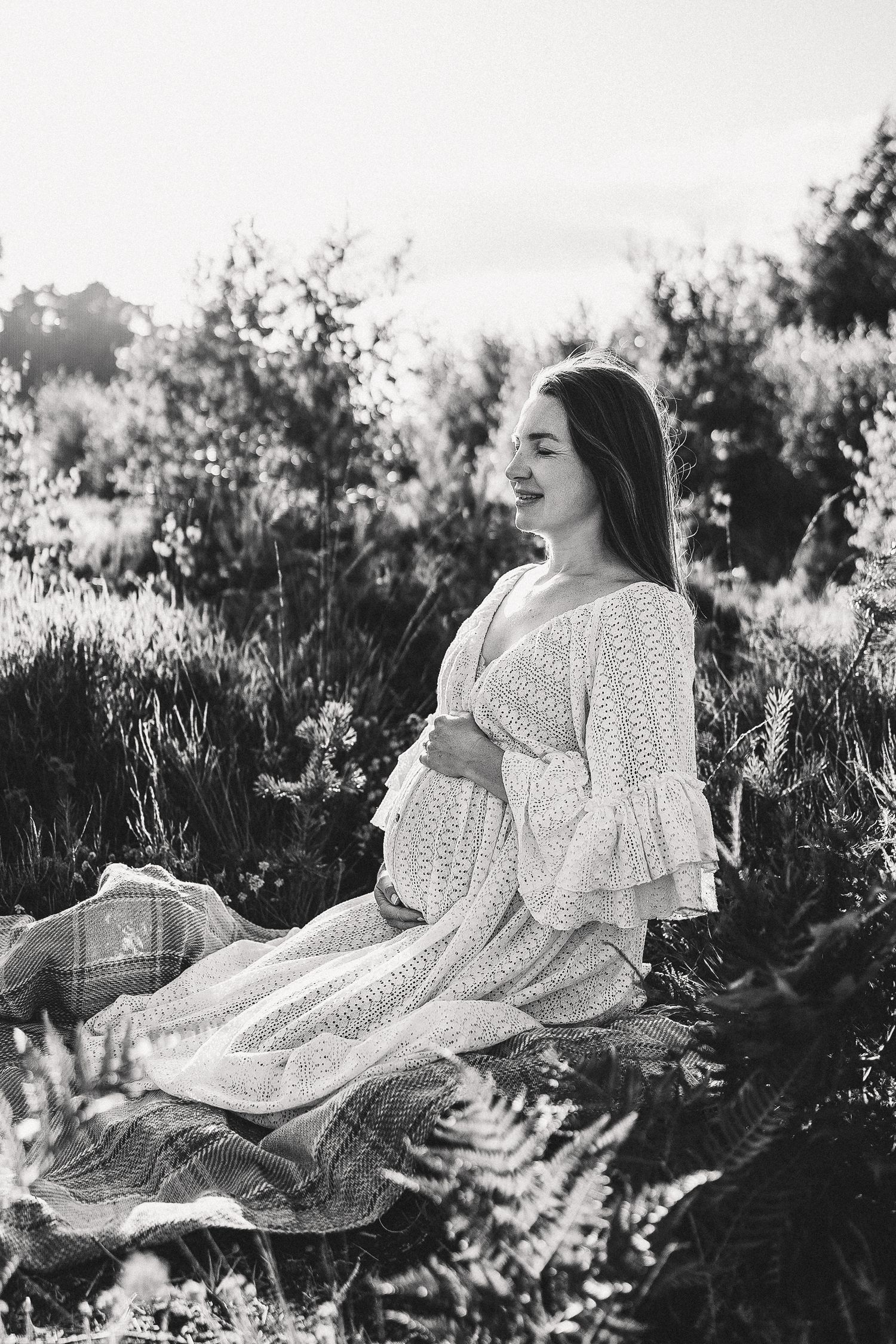 Woman in white lace dress sitting in a wildflower field during golden hour.