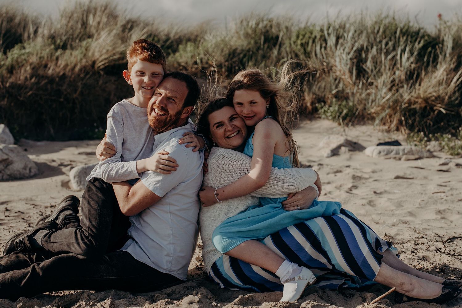 A loving family embraces while relaxing on a sandy beach during golden hour.