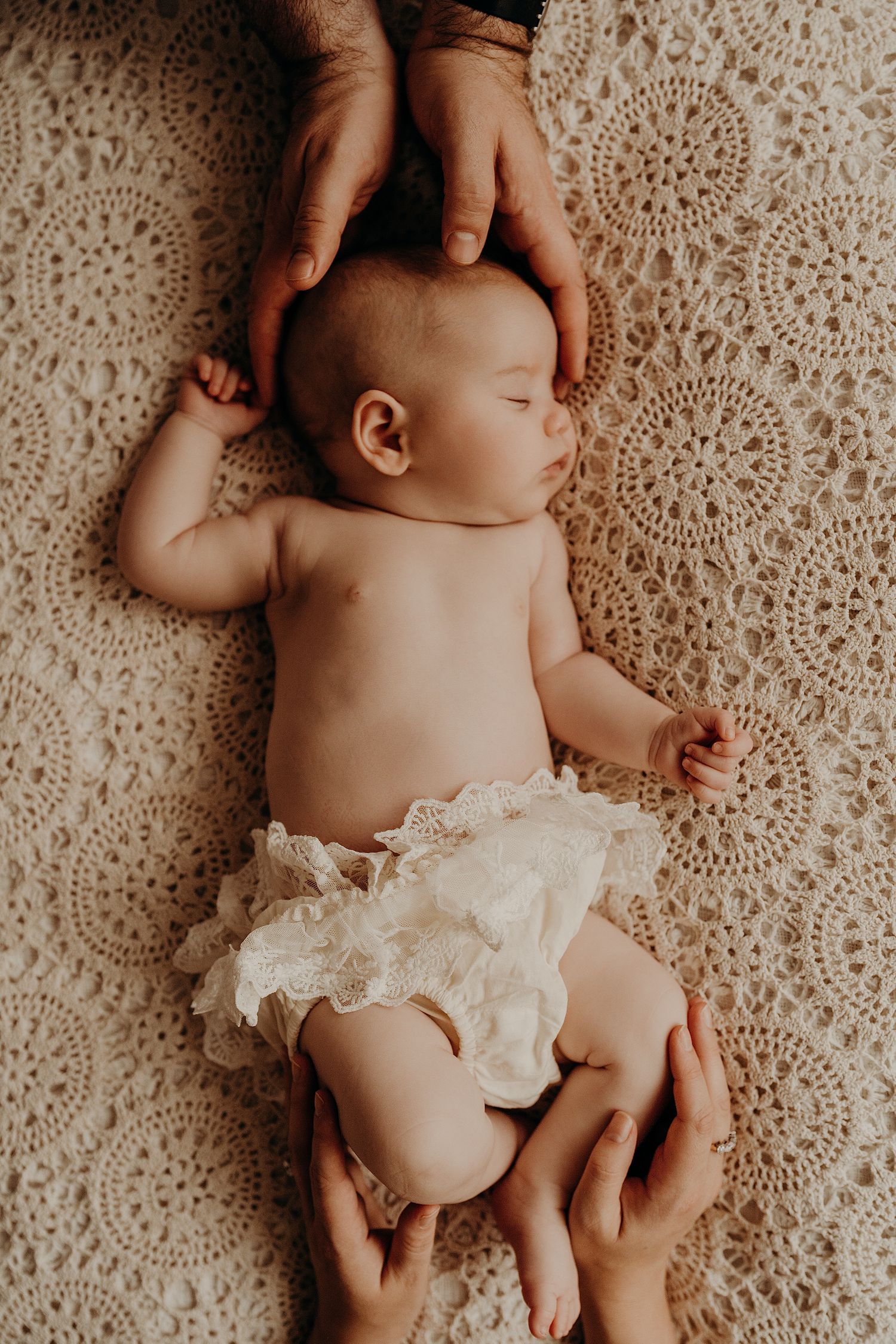 Newborn photography featuring delicate white lace details against a textured cream backdrop.