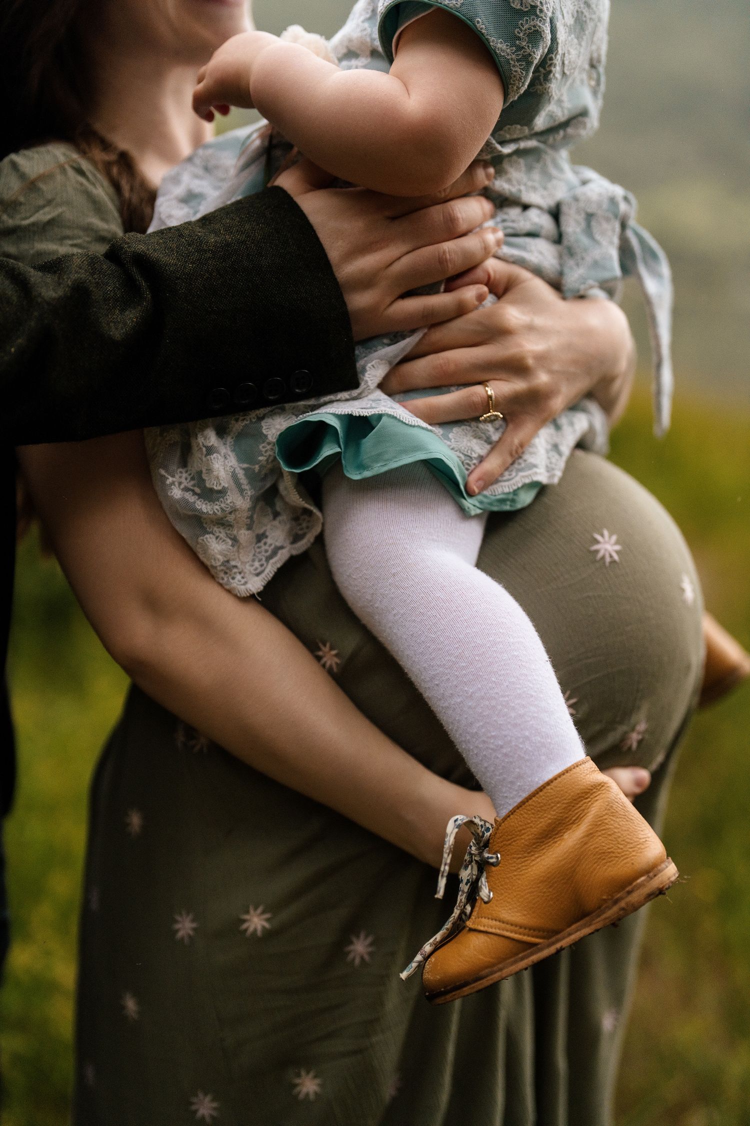 Close-up view of tiny brown leather baby shoes and white socks against a dark green dress.