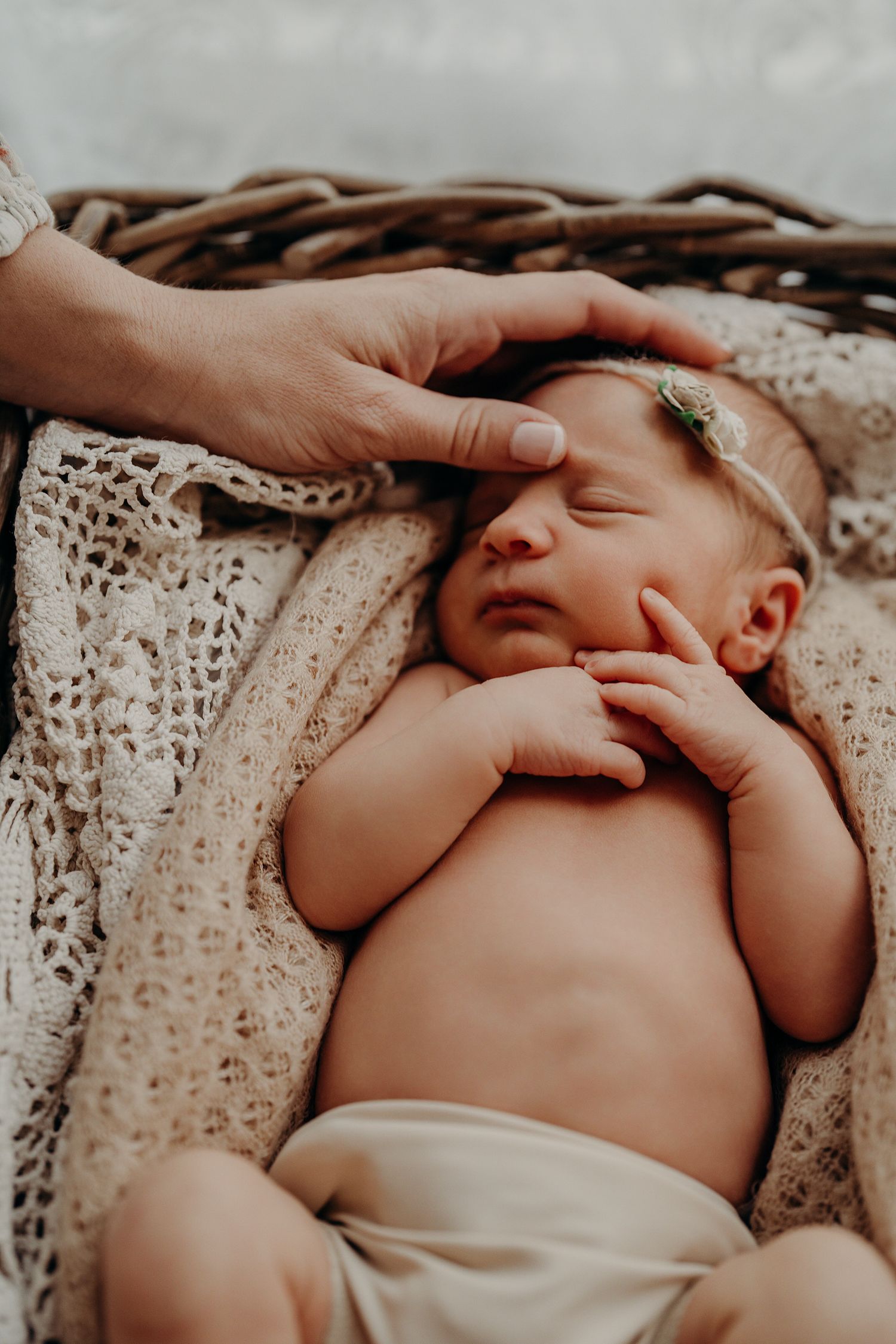 Gentle hands caress a sleeping newborn baby wrapped in delicate lace fabric.