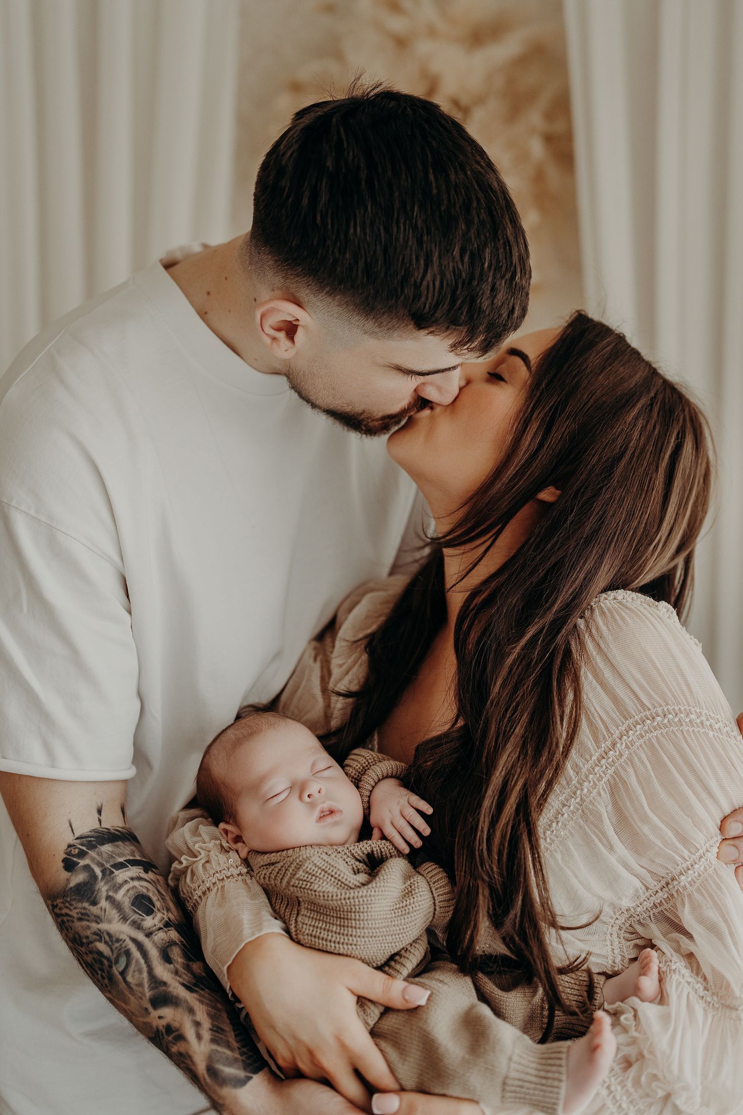 Lifestyle newborn photography Dublin parents kissing and cuddling baby in natural light studio