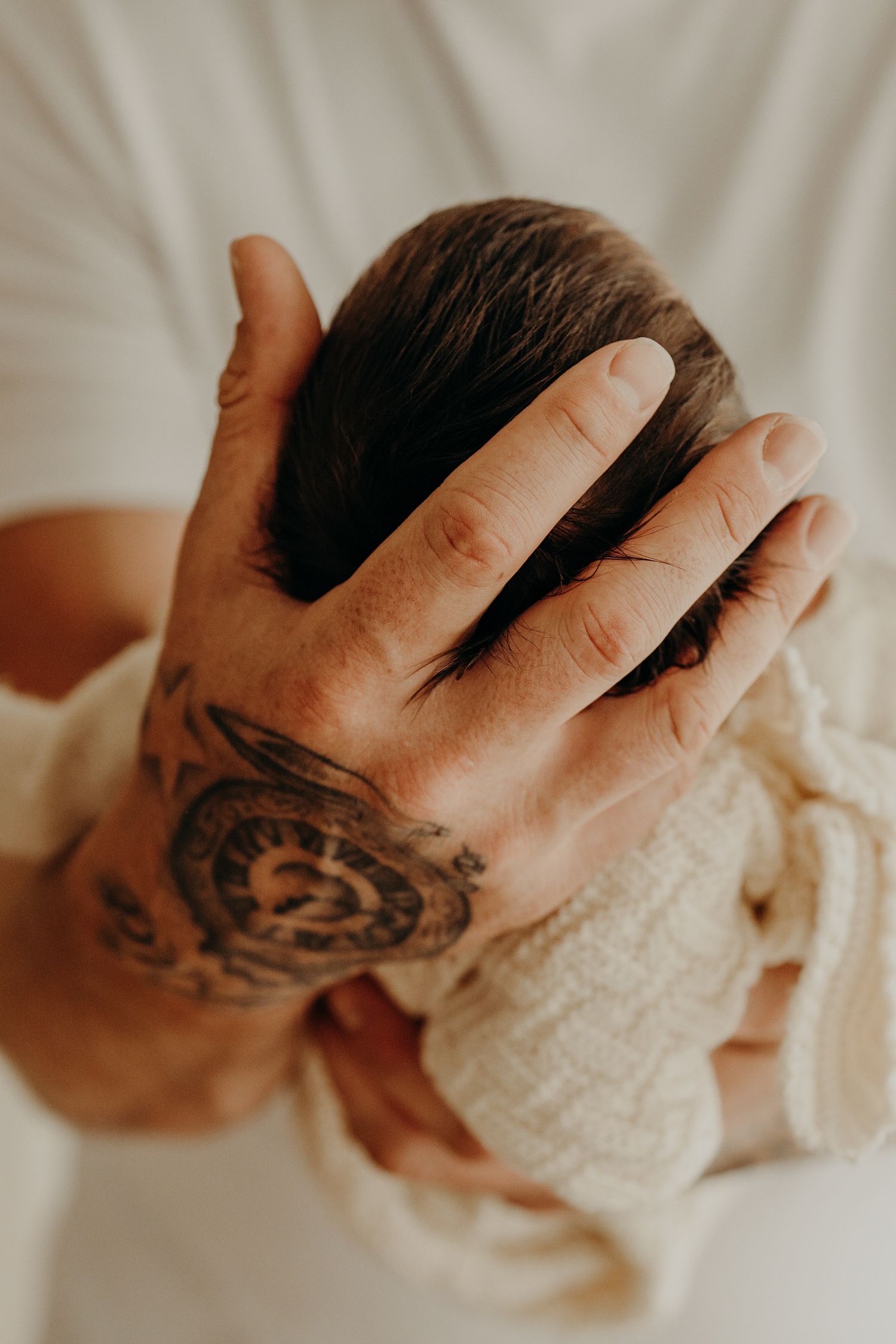 Gentle hands cradling a sleeping newborn wrapped in soft white fabric.