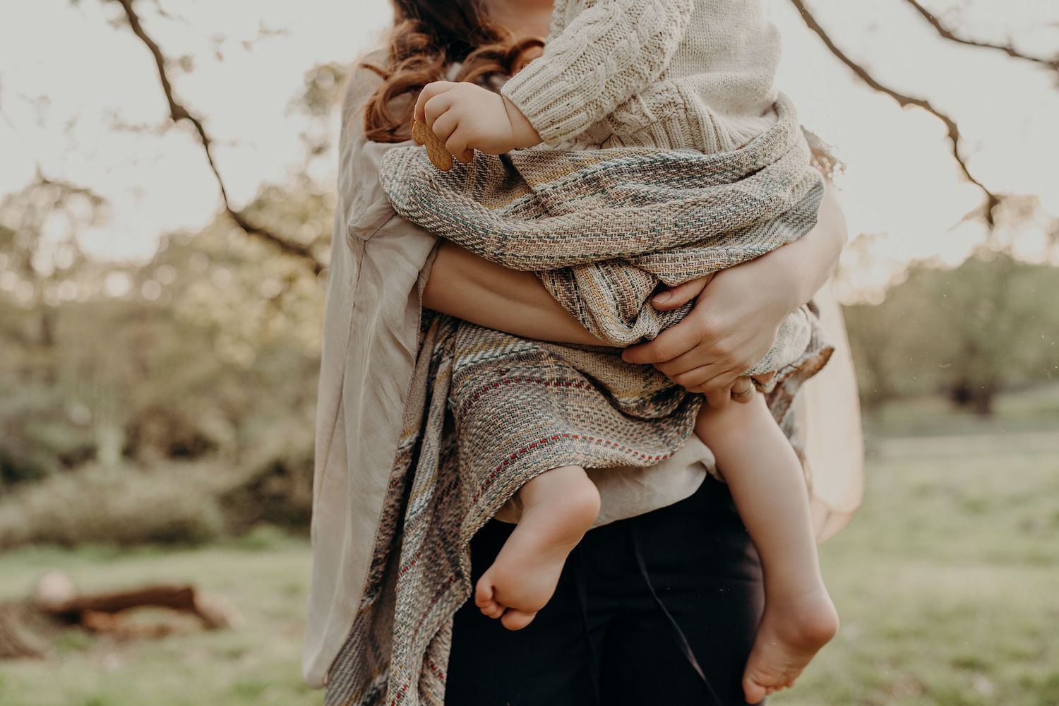 A loving family moment captured in warm sunlight wearing coordinated neutral tones on a grassy path.