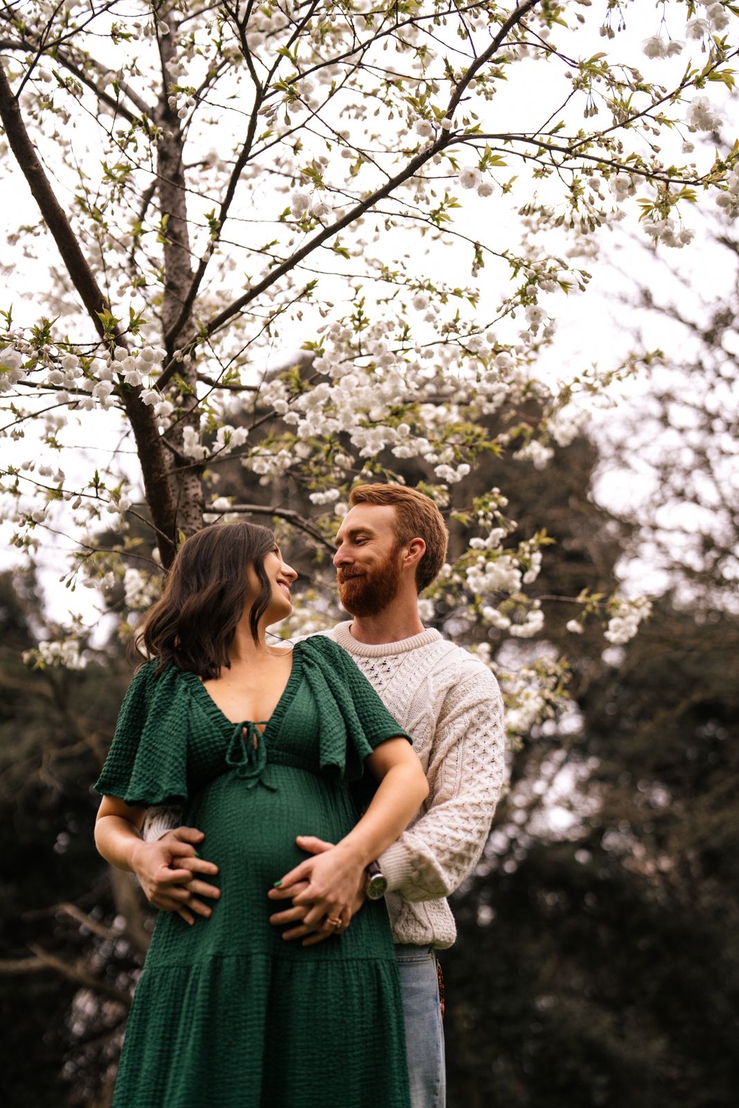 A couple embracing in a garden surrounded by blooming trees and flowers.