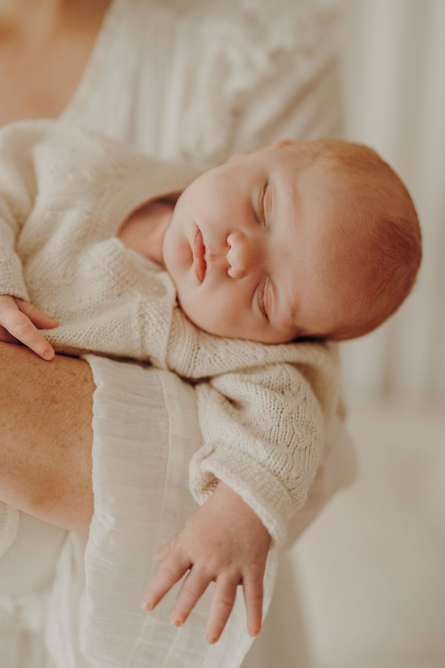 Sleeping newborn wrapped in cozy white knit blanket during professional photo shoot.