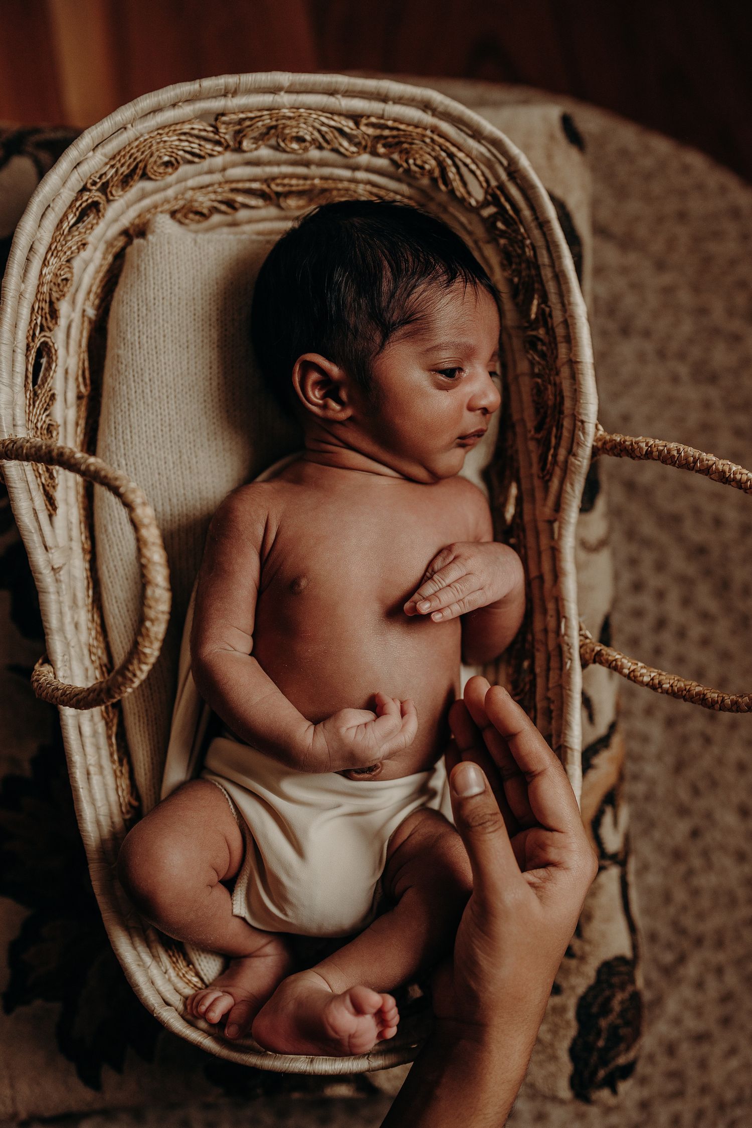 Sleeping infant resting peacefully in woven basket with gentle hands providing comfort.