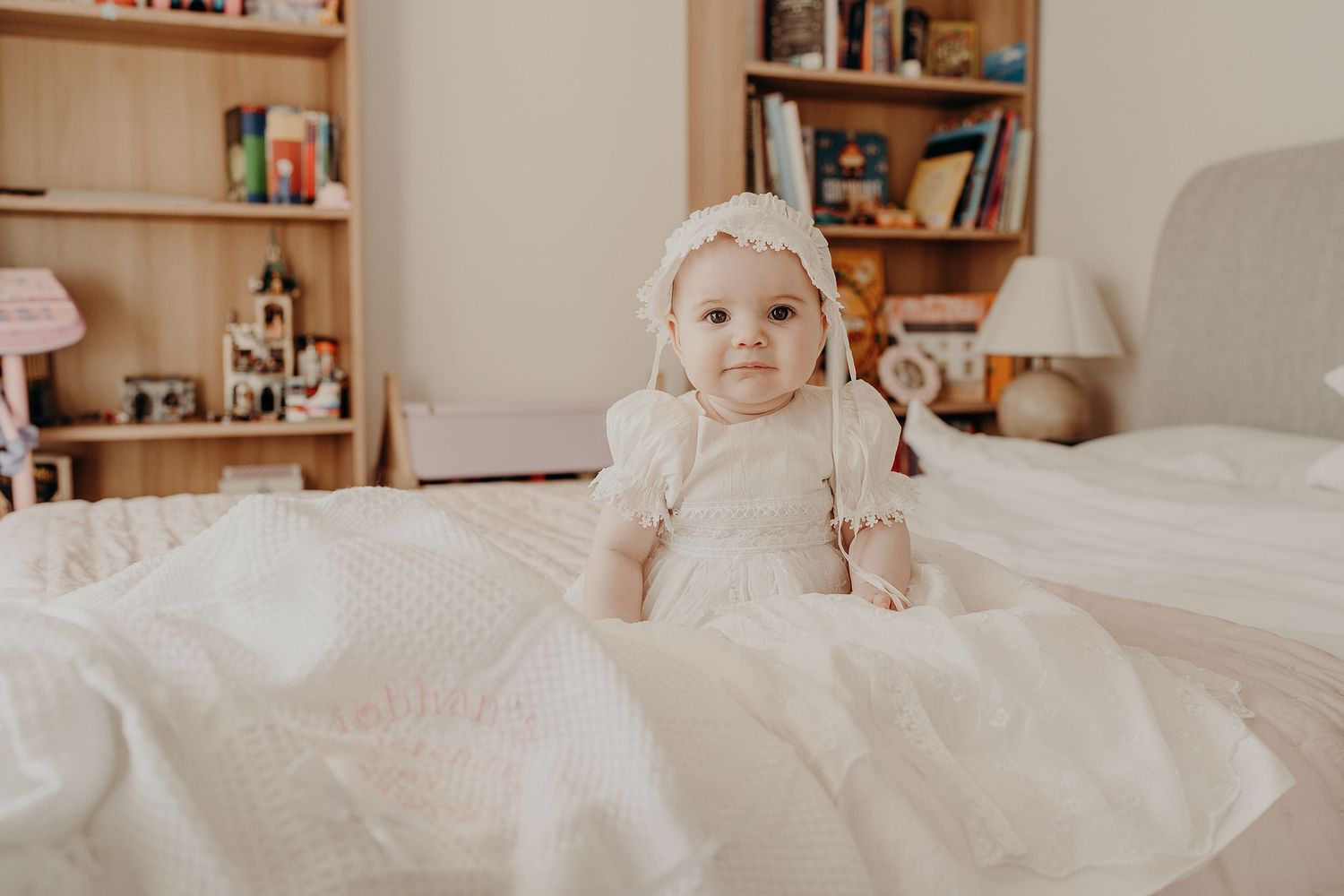 Soft white bedding and pillows arranged on a bed with wooden bookshelf in background.