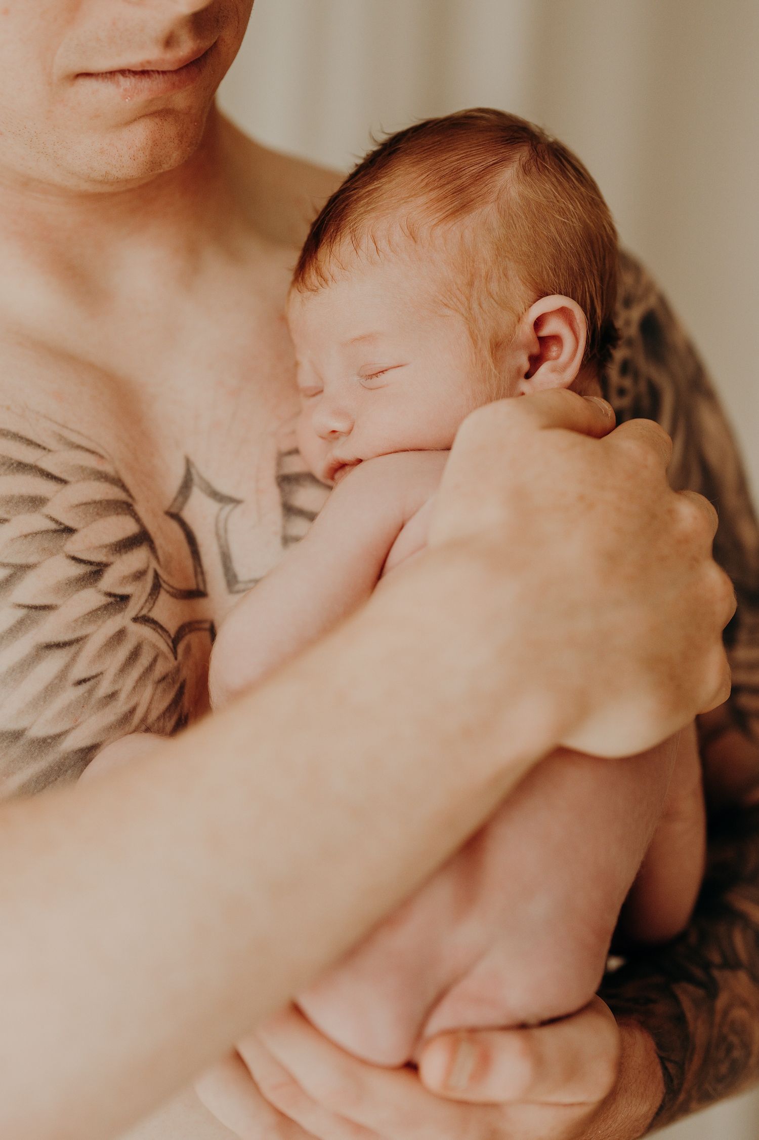Intimate close-up of a parent cradling a newborn baby against their chest.