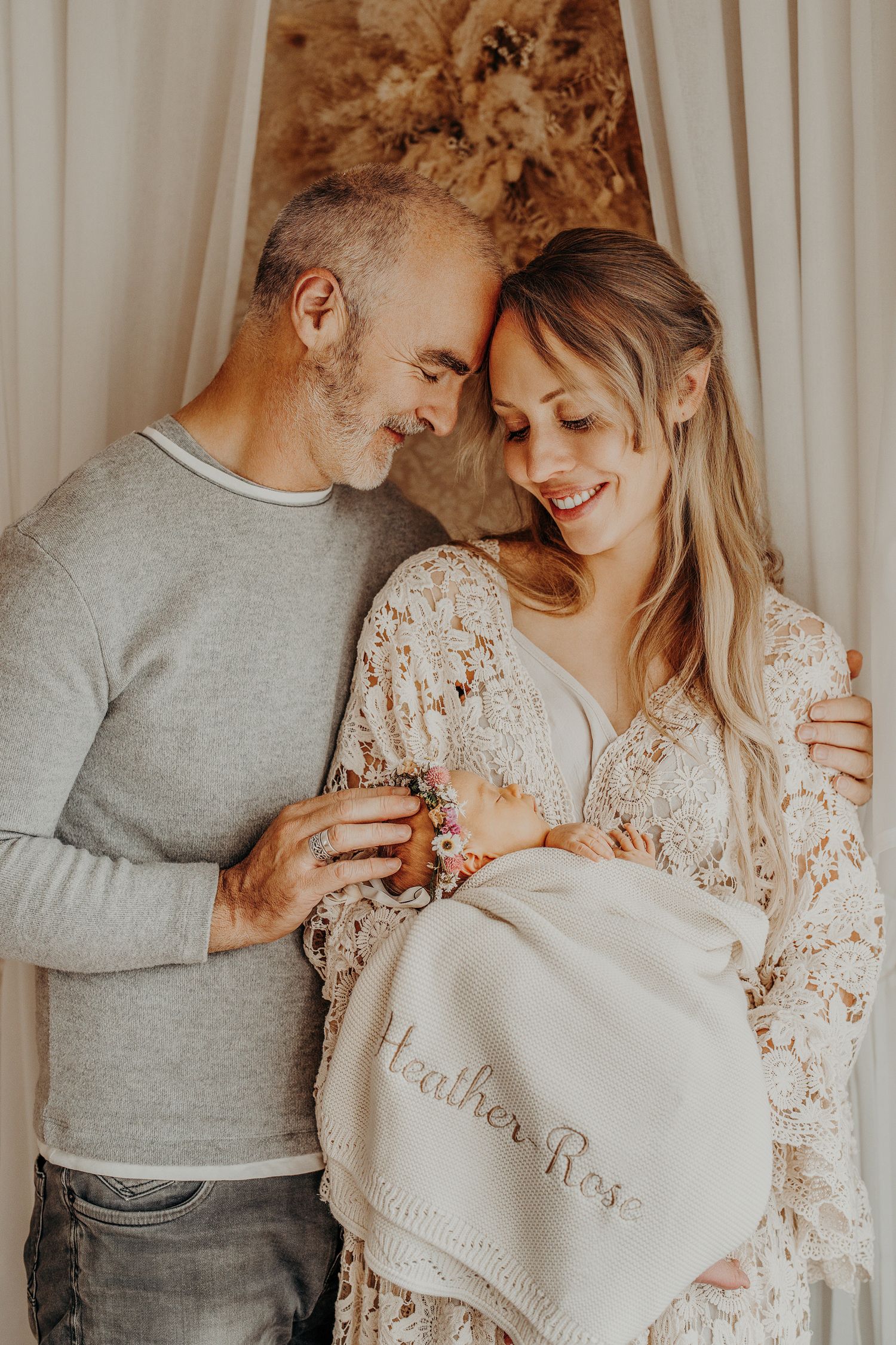 A tender moment captured of a couple holding a white embroidered blanket together in warm lighting.