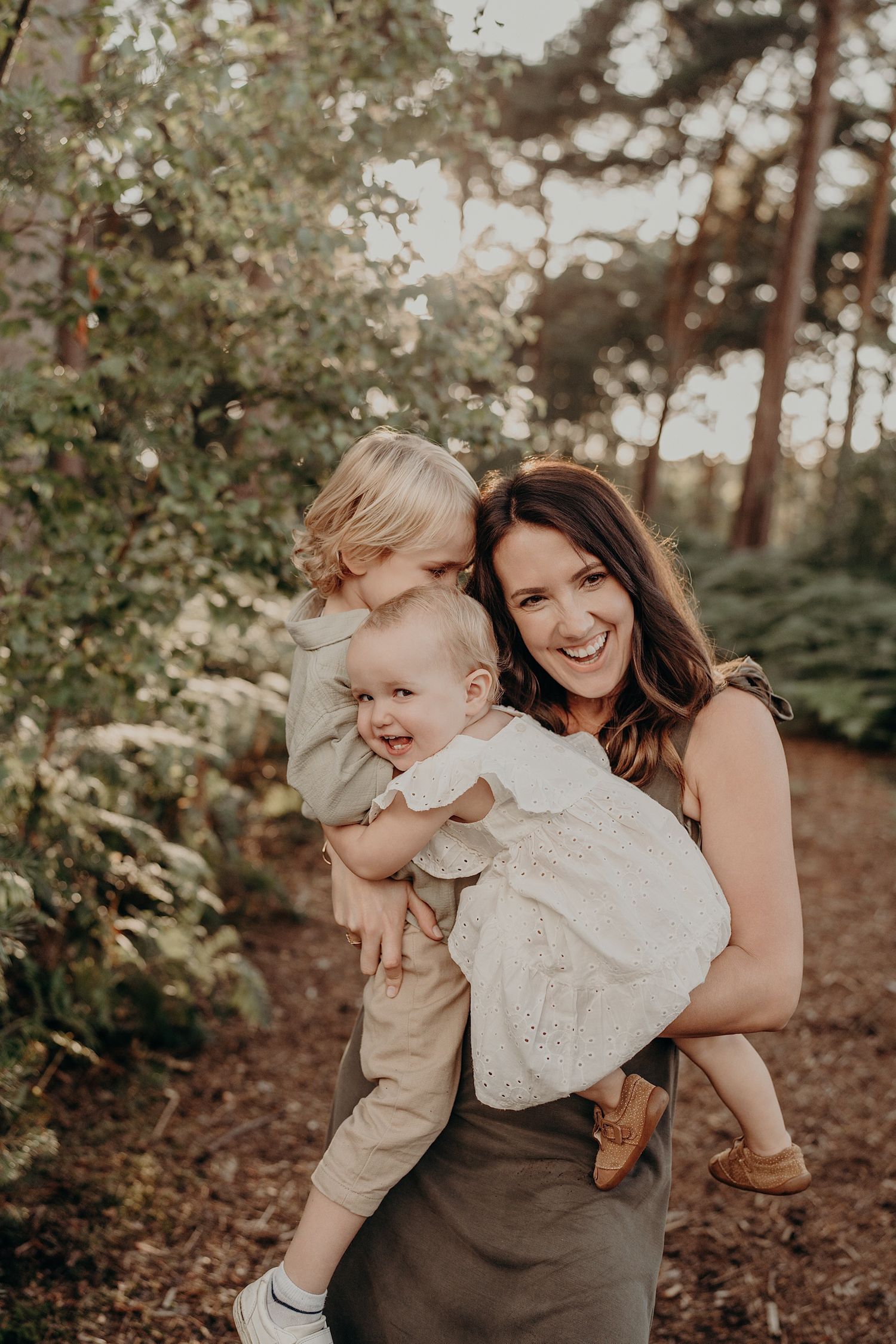 A joyful outdoor family photoshoot in a wooded setting with warm natural lighting and casual attire.