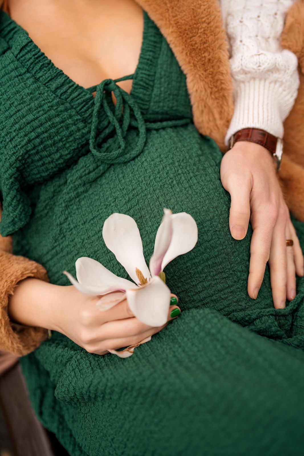 A person wearing a green sweater holds a white flower in their hands.