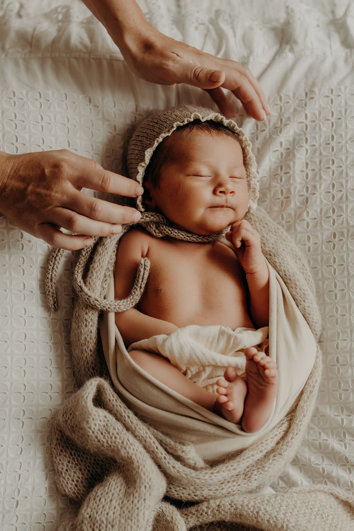 Sleeping infant wrapped in cozy knit blanket on textured white bedding.