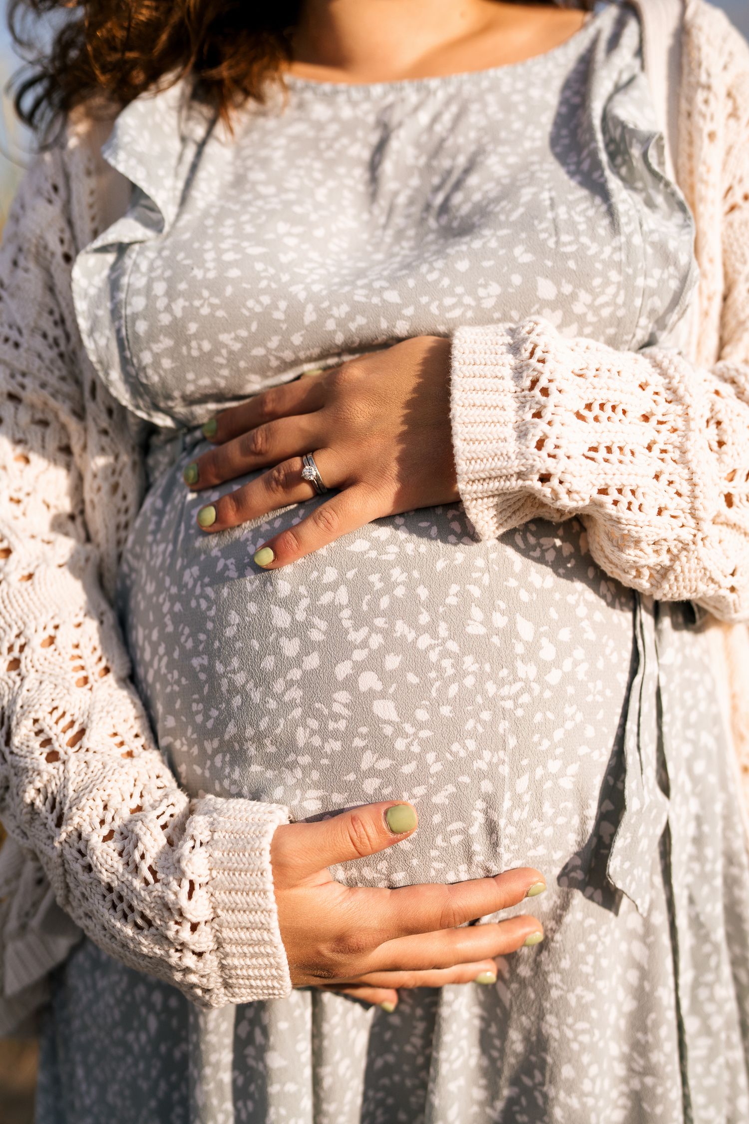 Close-up of hands cradling a pregnant belly in a gray polka dot dress and lace cardigan.