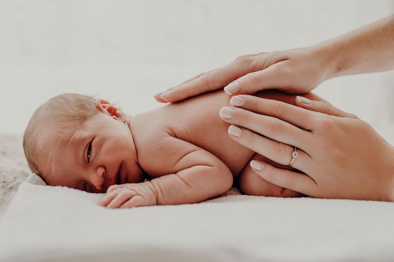 Delicate hands tenderly holding sleeping newborn during photo session.