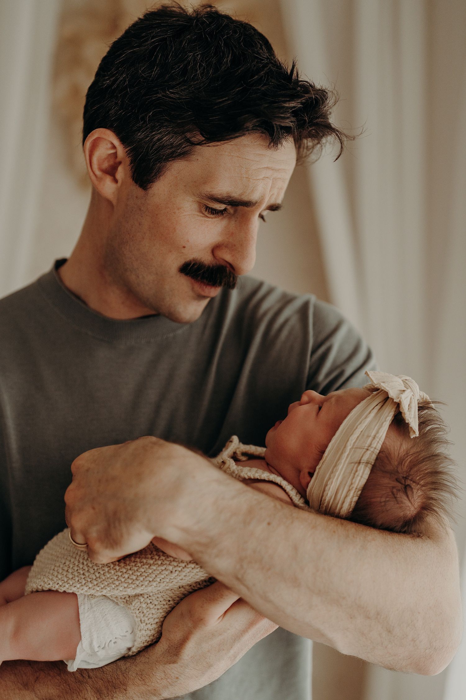 Tender moment between caregiver and newborn in soft window light.