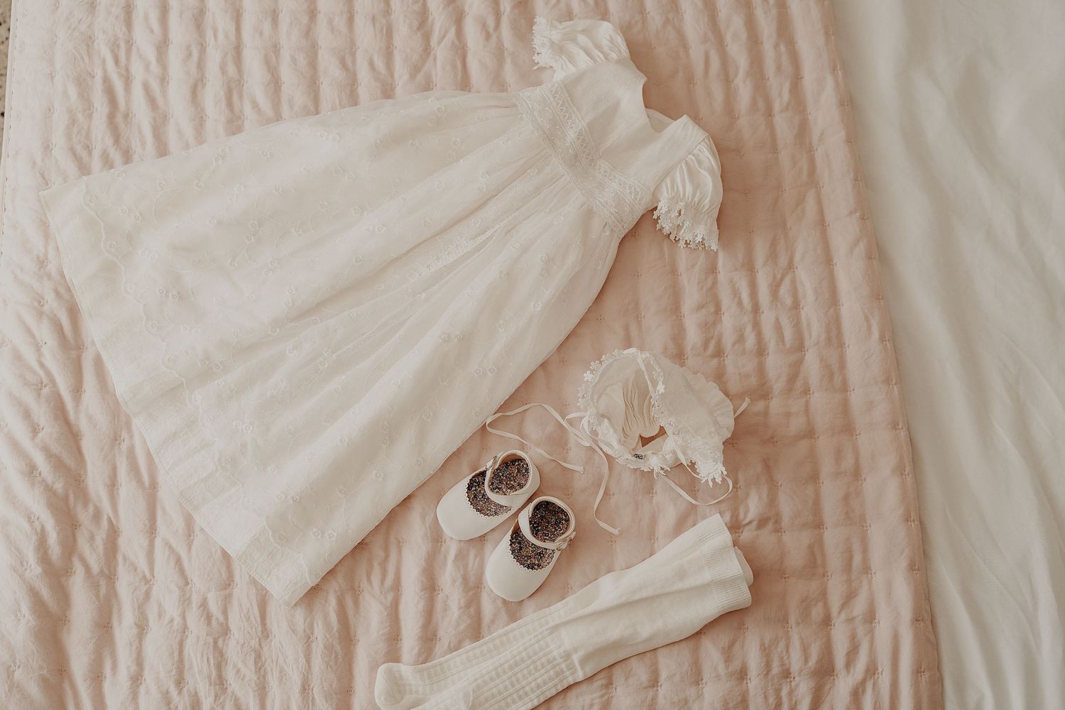 White christening gown laid flat on textured fabric showing intricate lace details.