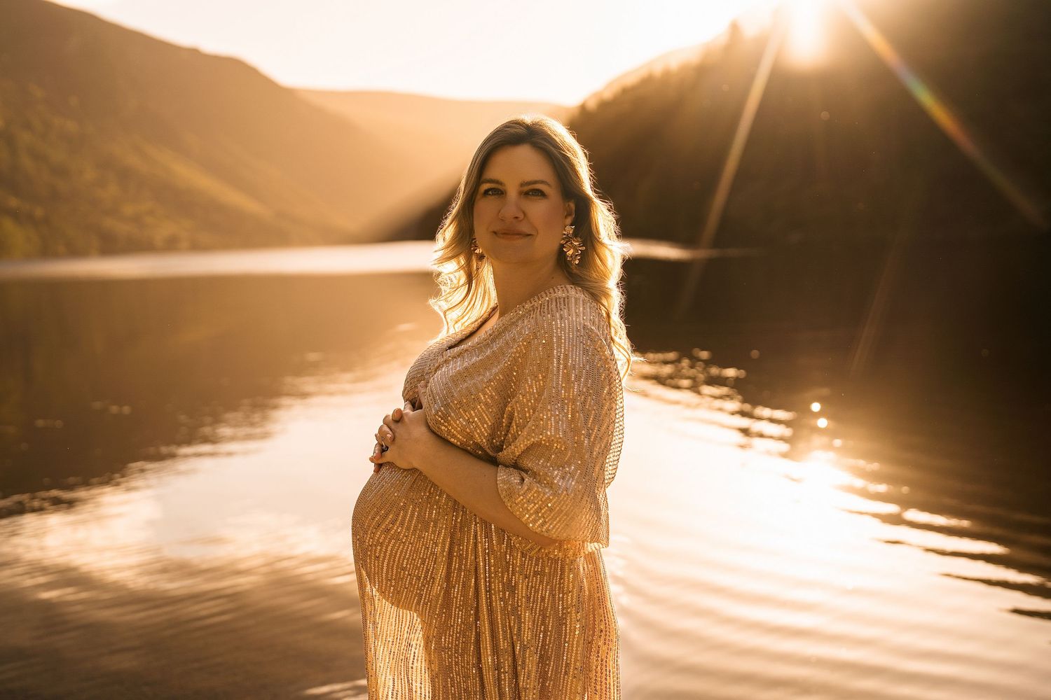 Maternity photography session at sunset by a lake in golden light.