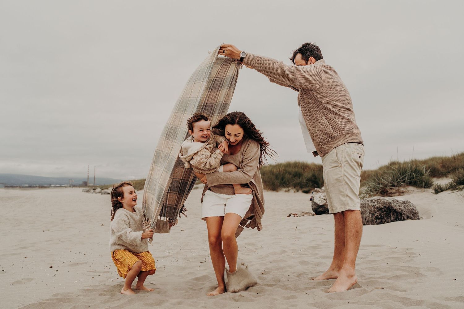 Family playing and running together on a sandy beach with dunes in the background.