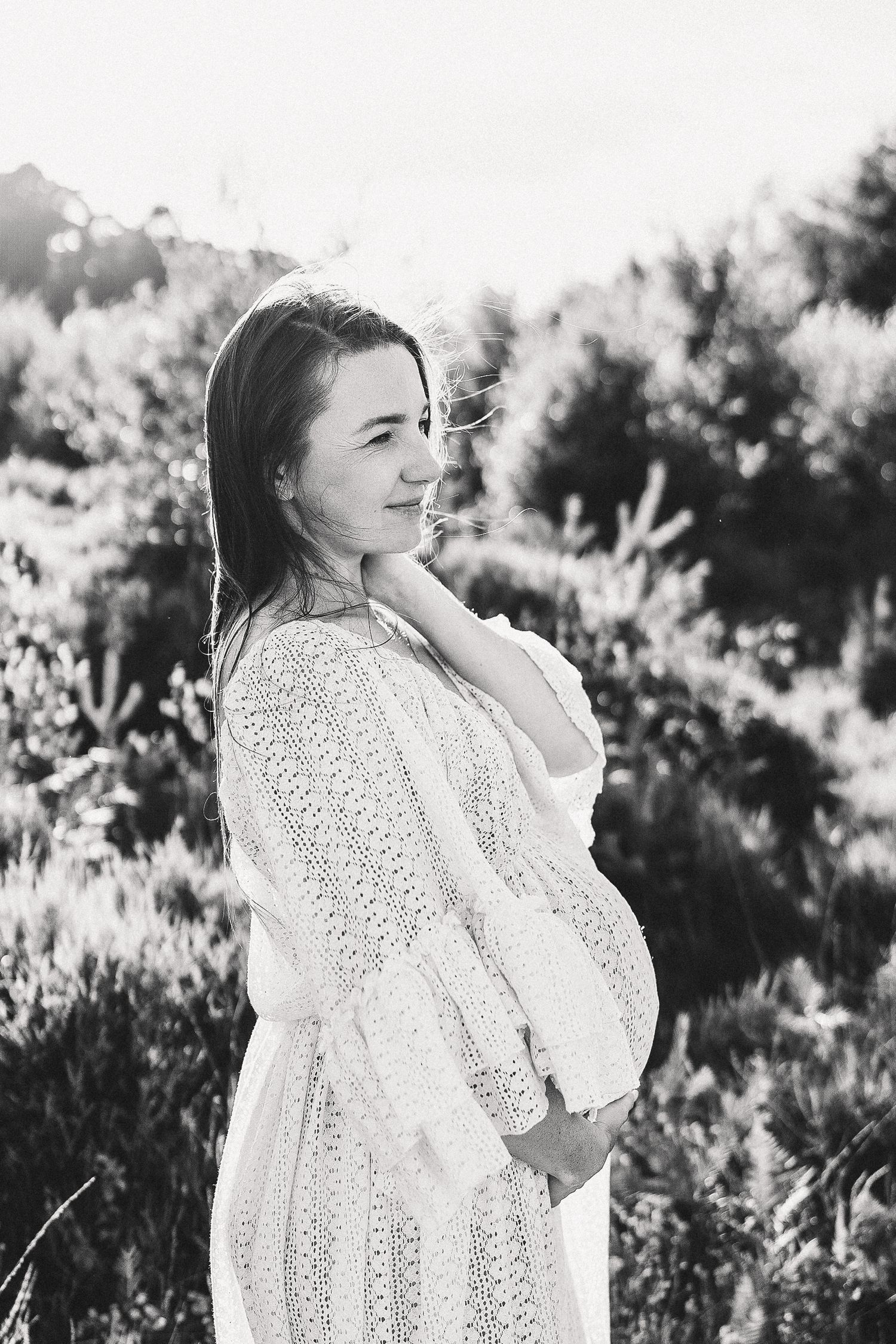 Black and white portrait of woman in floral dress sitting among wildflowers.