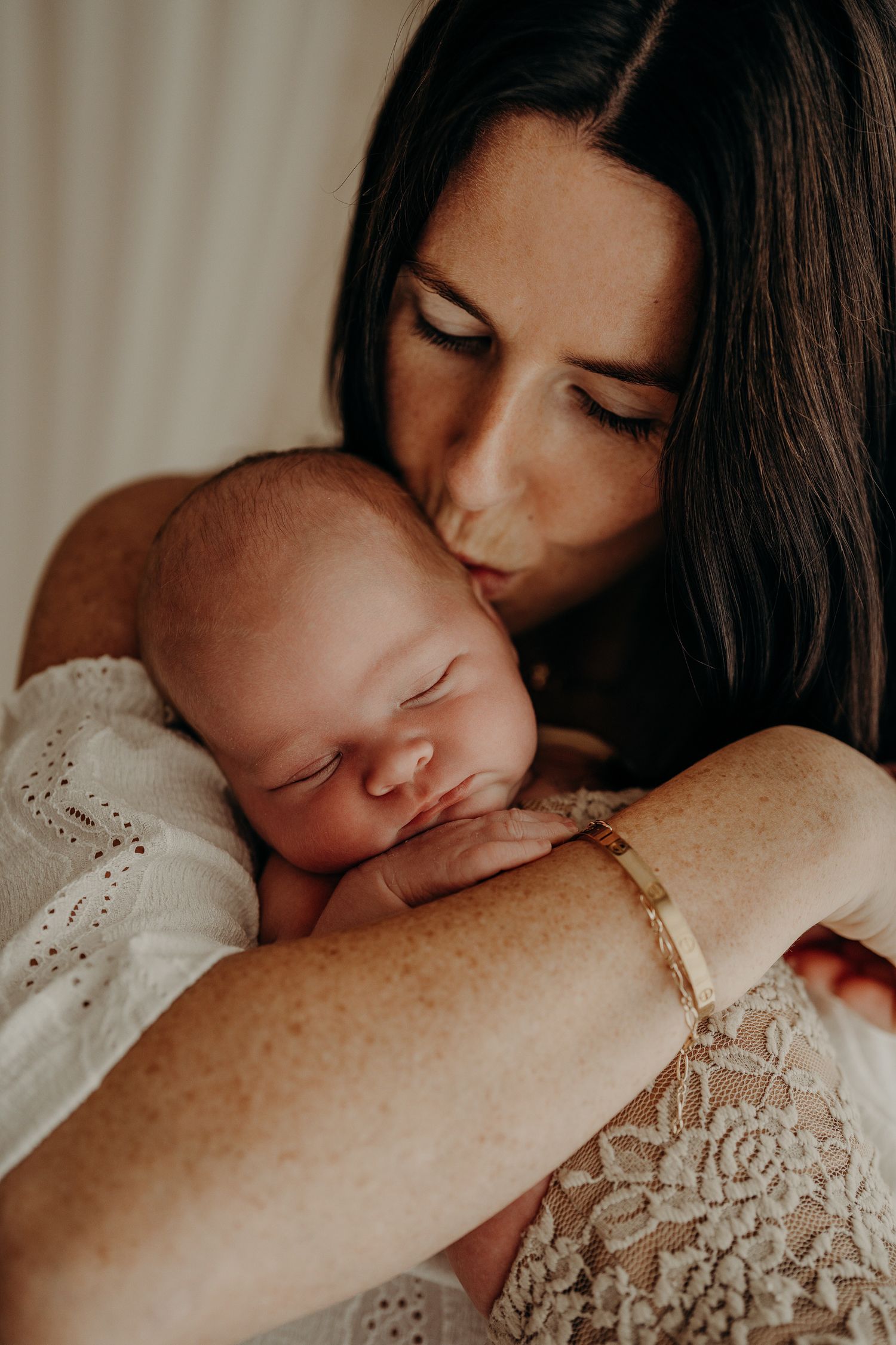 A tender moment captured as a parent kisses their sleeping newborn baby while wearing a lace-detailed top.