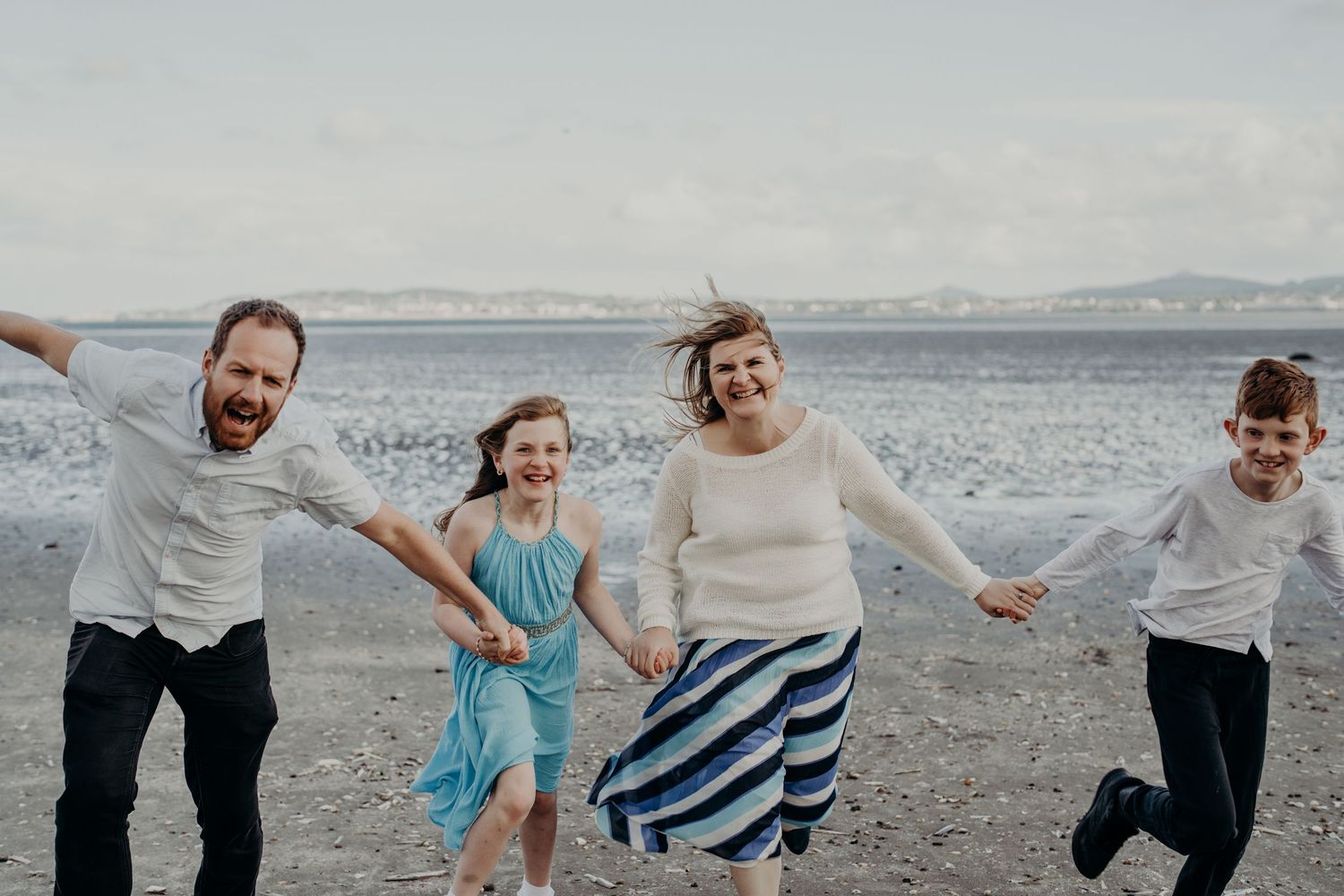 Family running and playing together on a scenic beach with mountains in the distance.