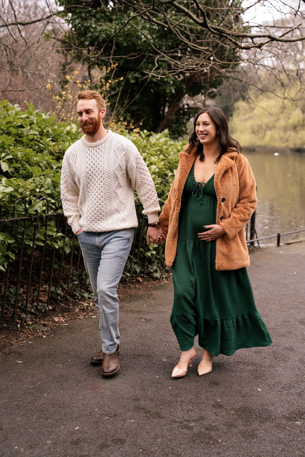 A pregnant woman and her partner walking together on a path in a wooded area.