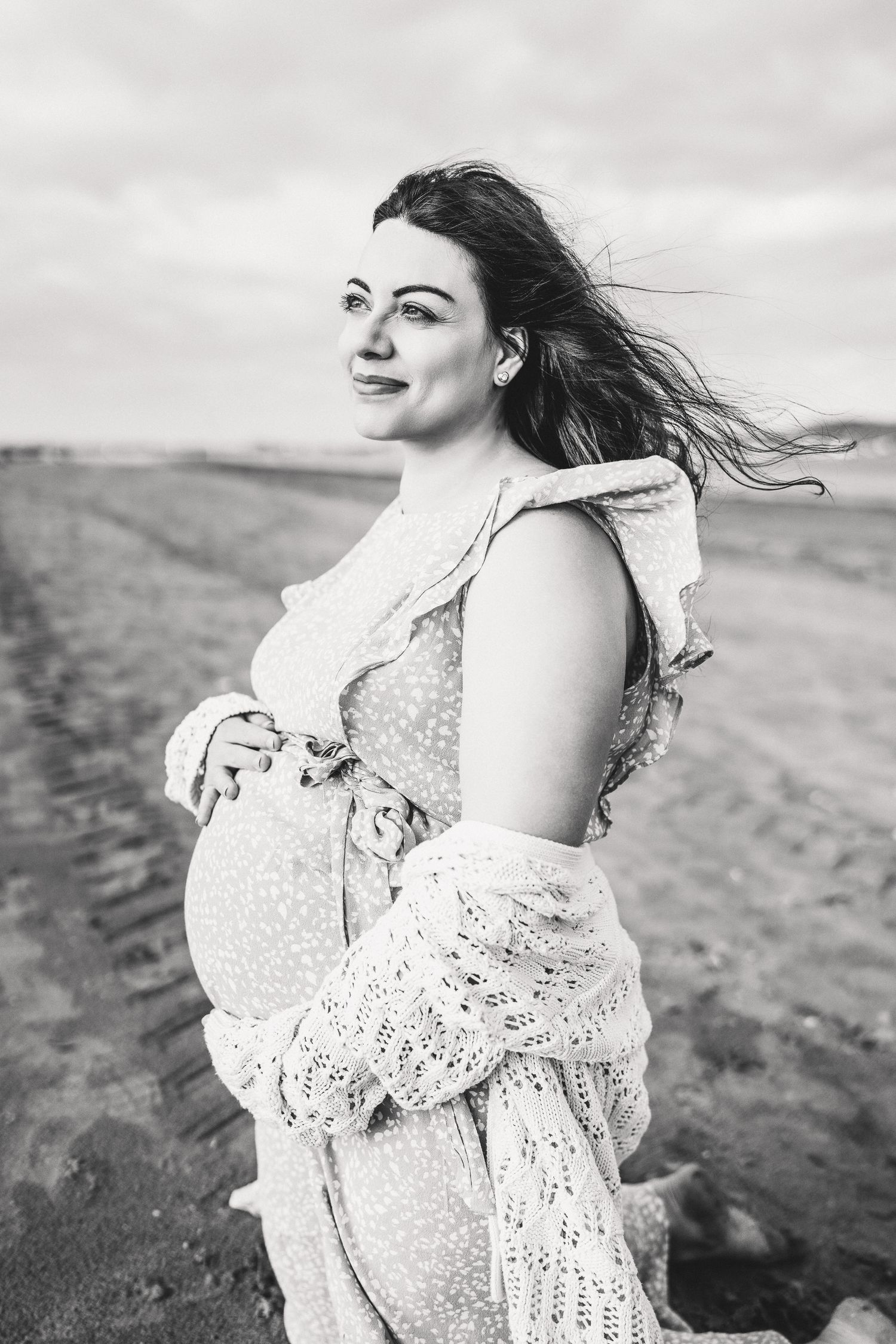 Woman in flowing white dress standing on hillside with hair blowing in the wind.