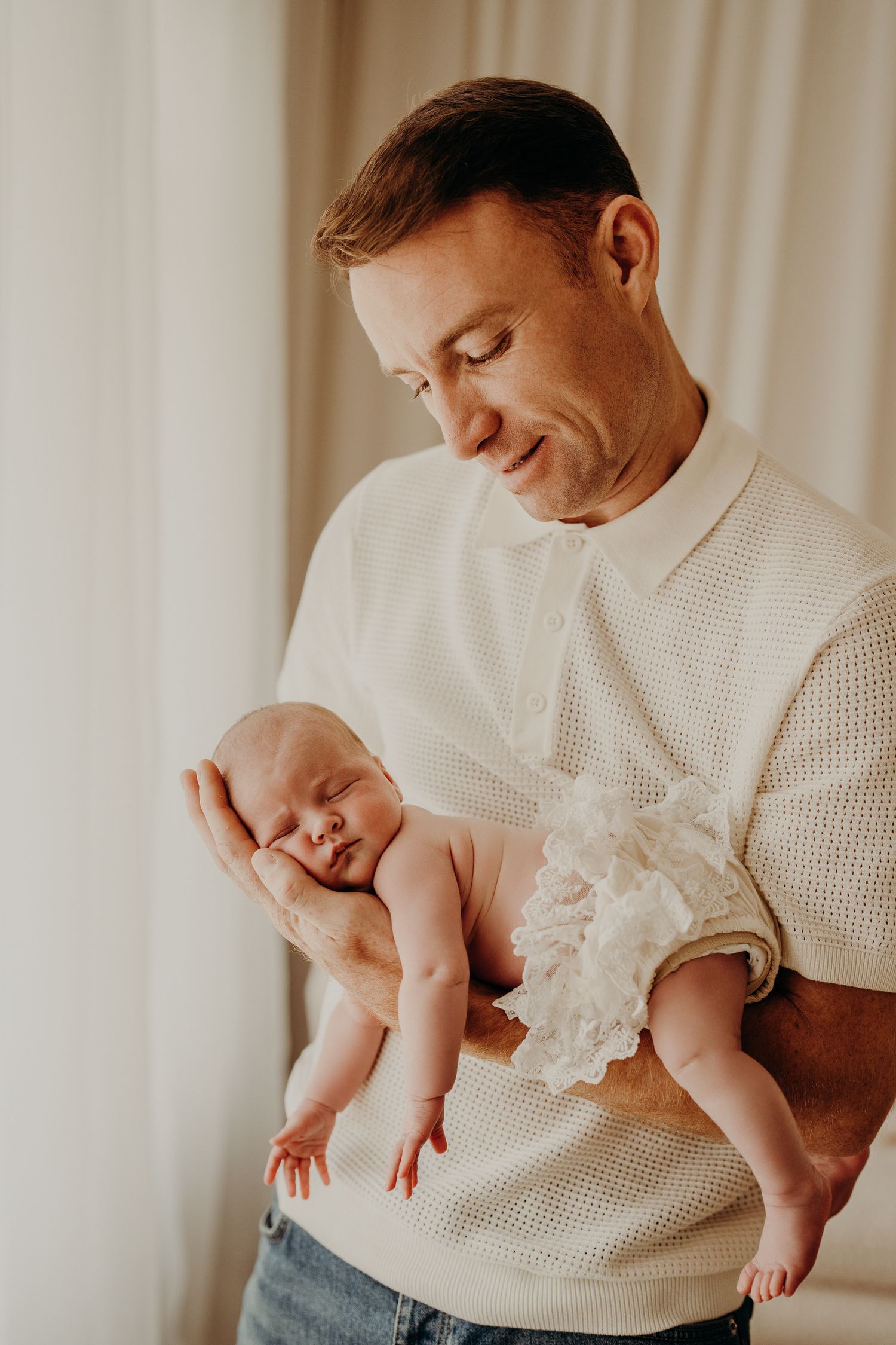 A parent in a white sweater tenderly holds their sleeping newborn baby against a light background.
