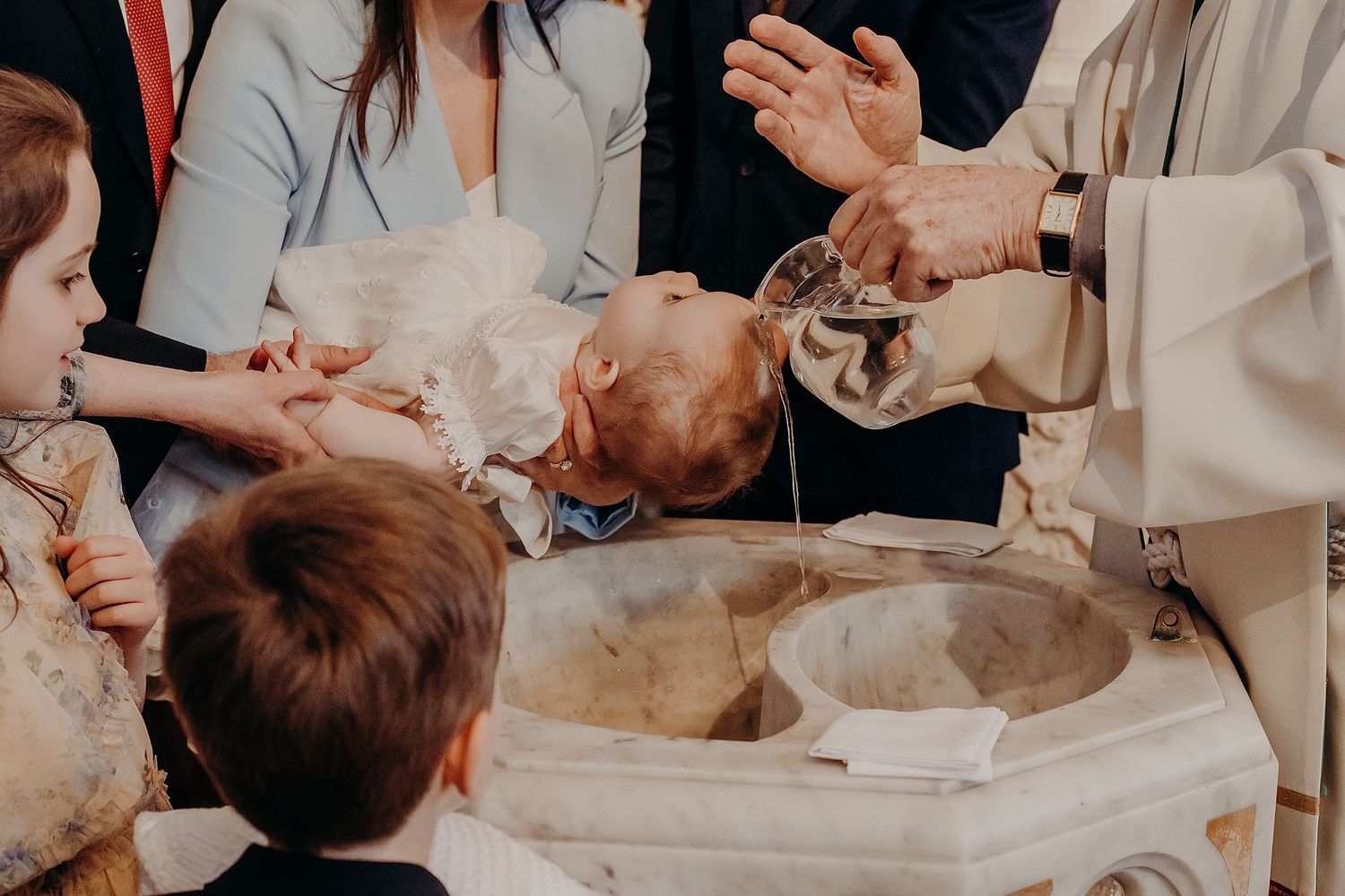 Gathering of family members around baptismal font during religious ceremony.
