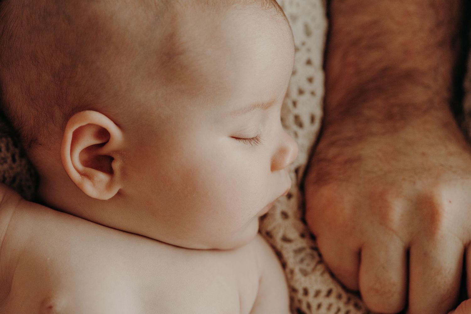 Gentle close-up photo of a sleeping newborn baby wrapped in soft blankets.
